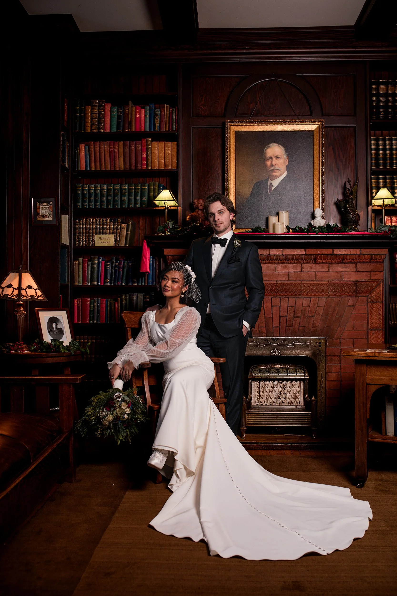 Rutherford House Wedding in Edmonton, Alberta. Couple poses with fireplace and chair.