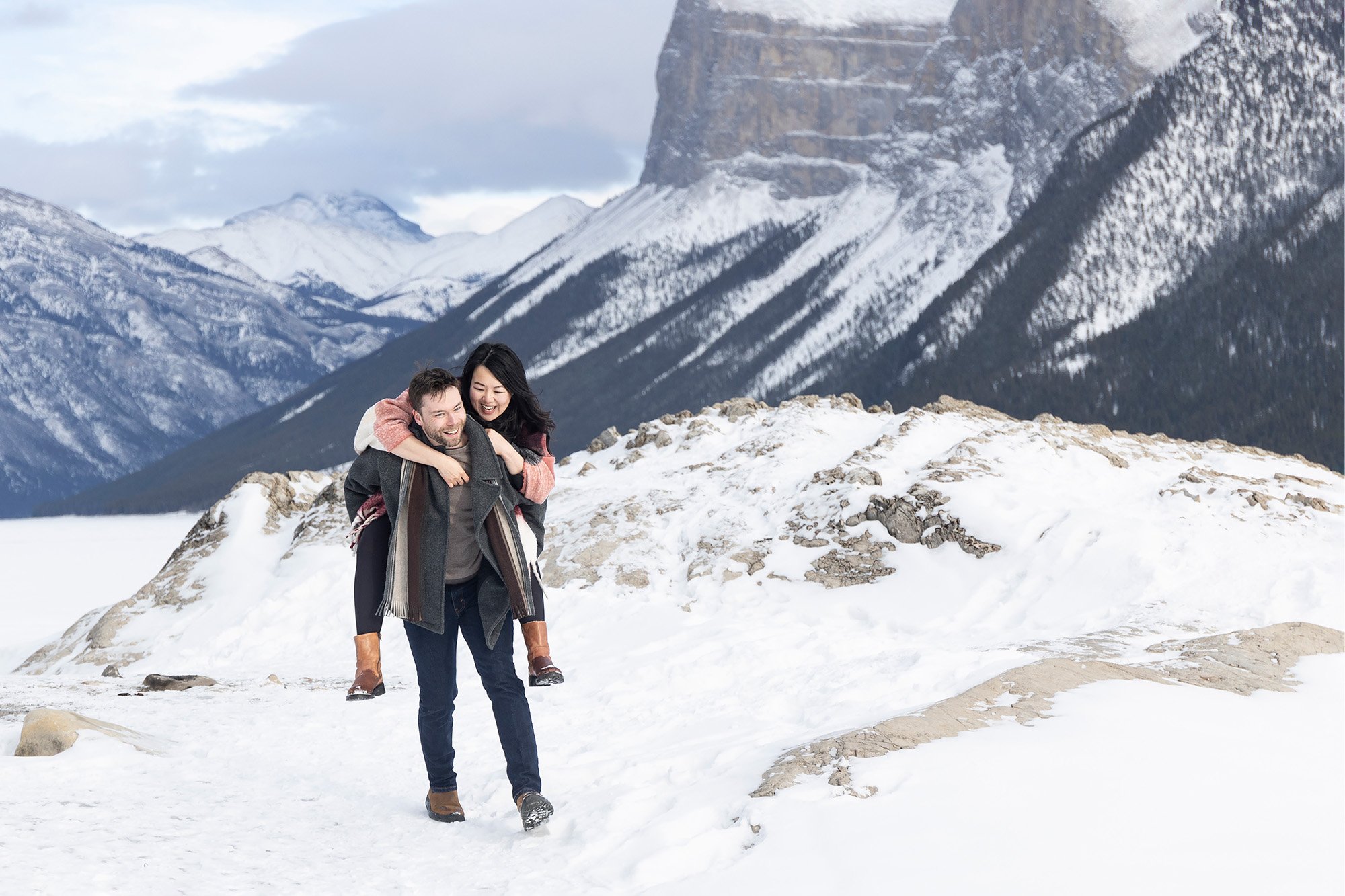 Man gives Women piggyback during engagement shoot at Lake Minnewanka in Banff