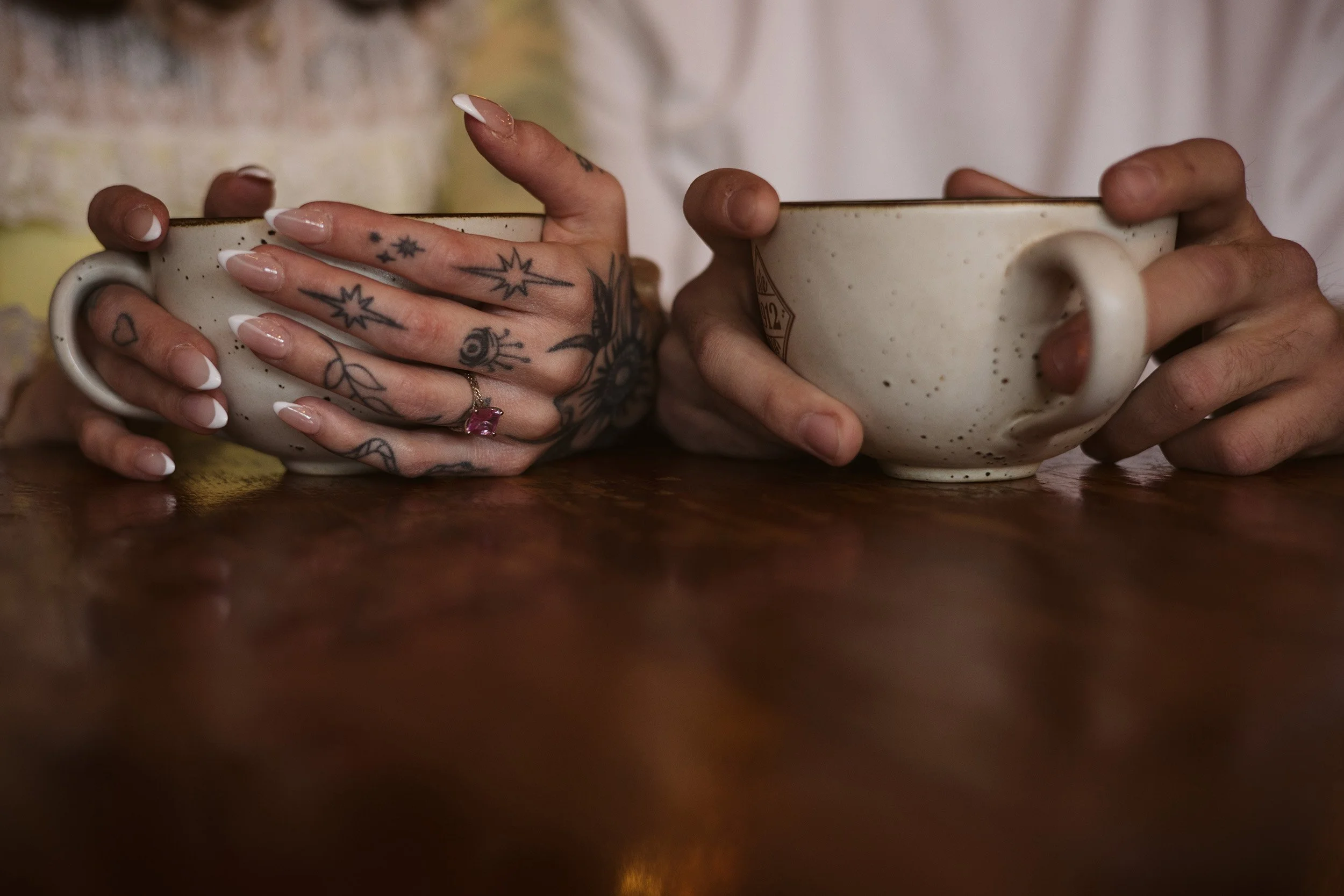 Alternative couple photo shoot close-up of couples hands on coffee cups with pink engagement ring