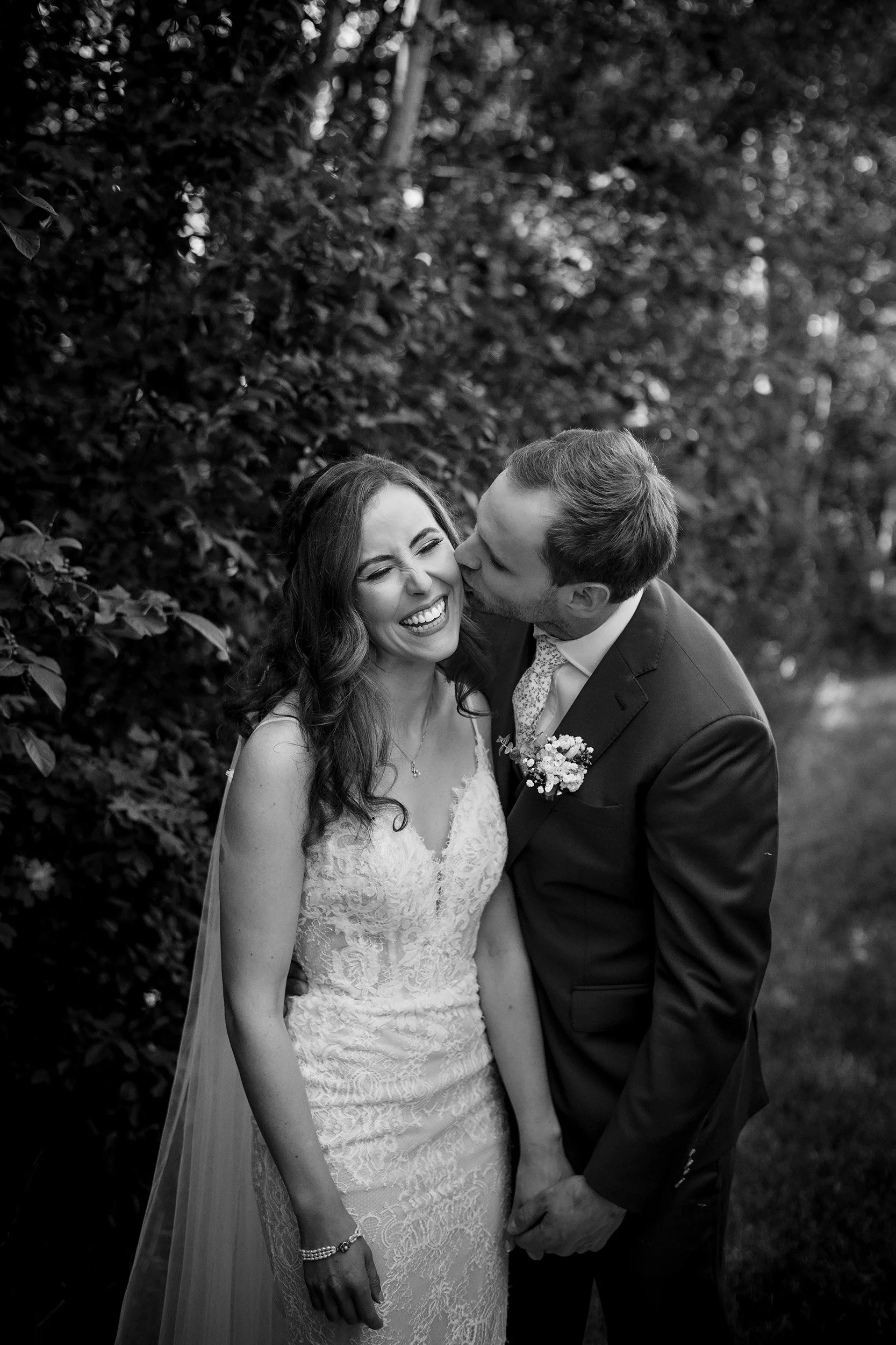 Groom kisses Bride on cheek in black and white photo taken at Gardenview Estates wedding venue