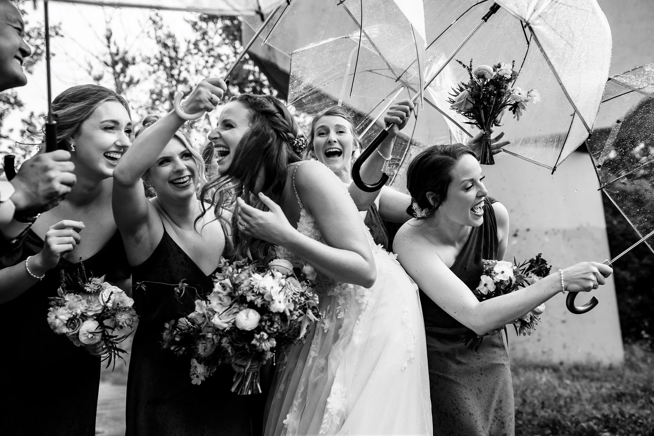 Wedding party hide under umbrellas during rain storm 