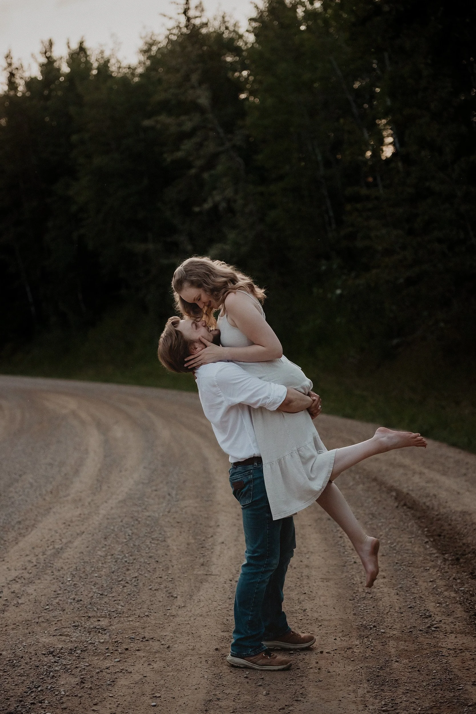 Couples photos on dirt road where he is picking her up at dusk