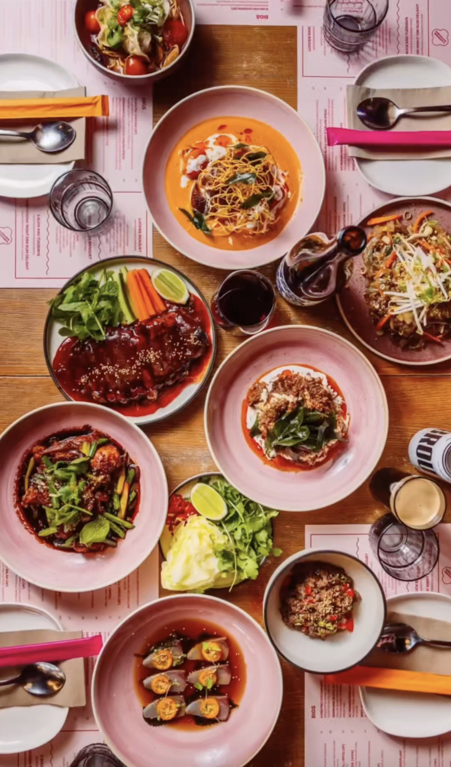 A variety of Asian dishes on a wooden table, including soups, salads, and rice dishes, with drinks and utensils.
