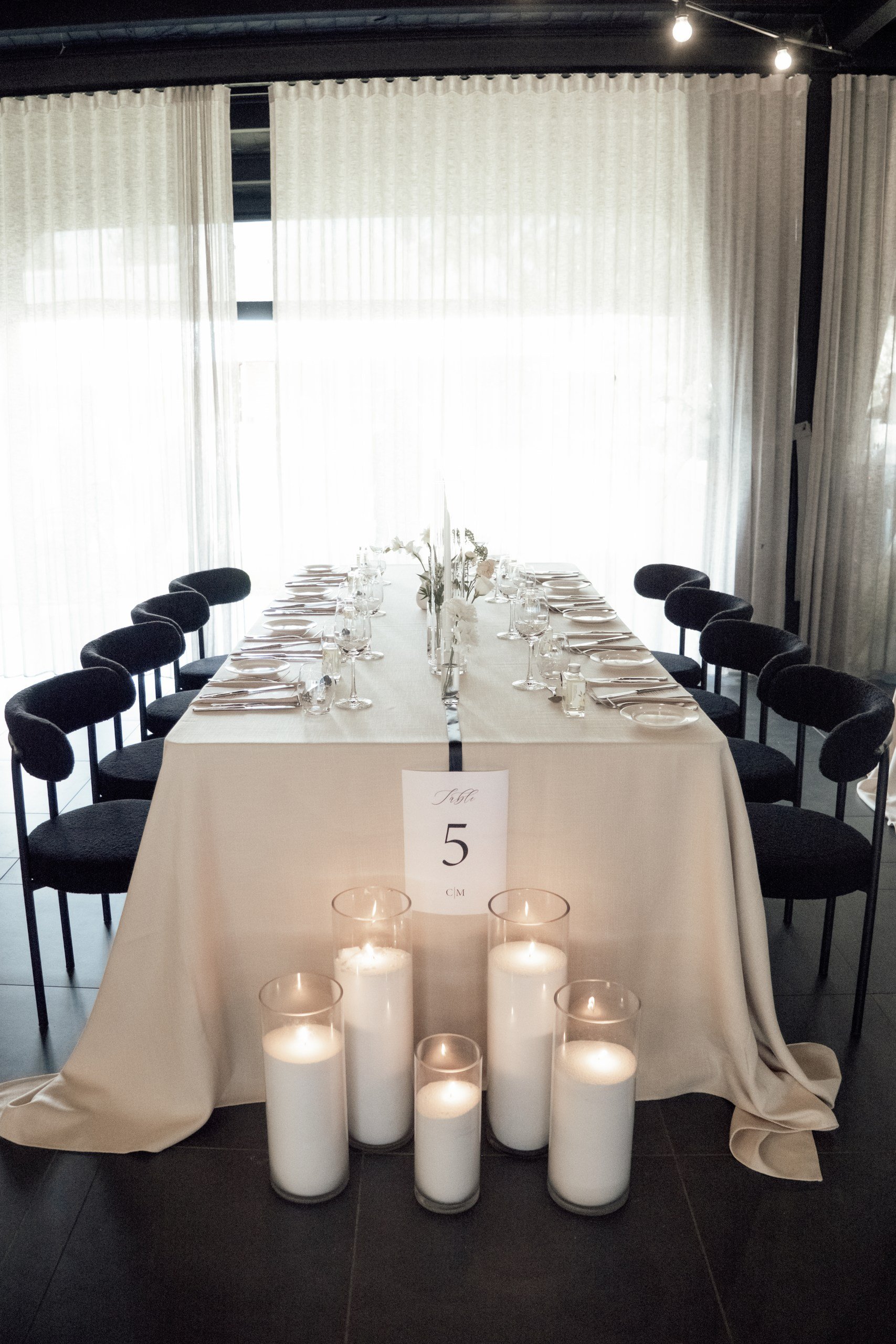 Modern wedding guest table featuring contemporary styling, white and green florals, black chairs and layered table details.