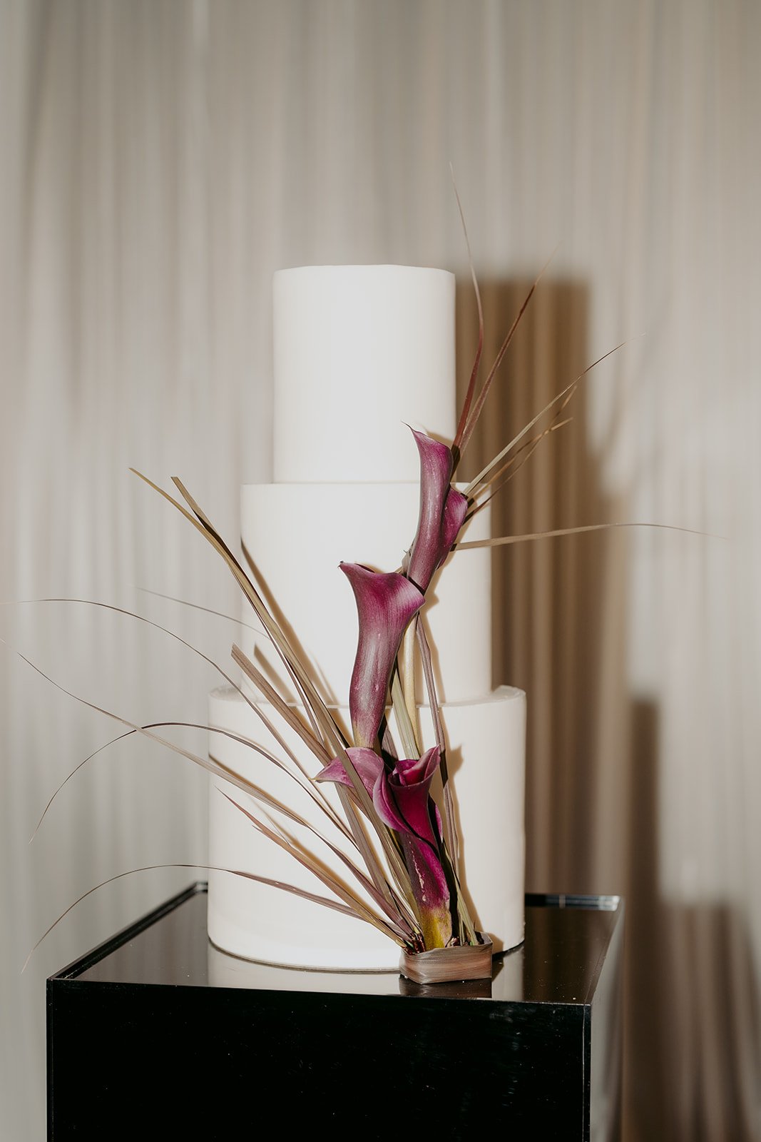 Modern wedding cake, three tier, smooth white icing and structured deep purple floral feature.