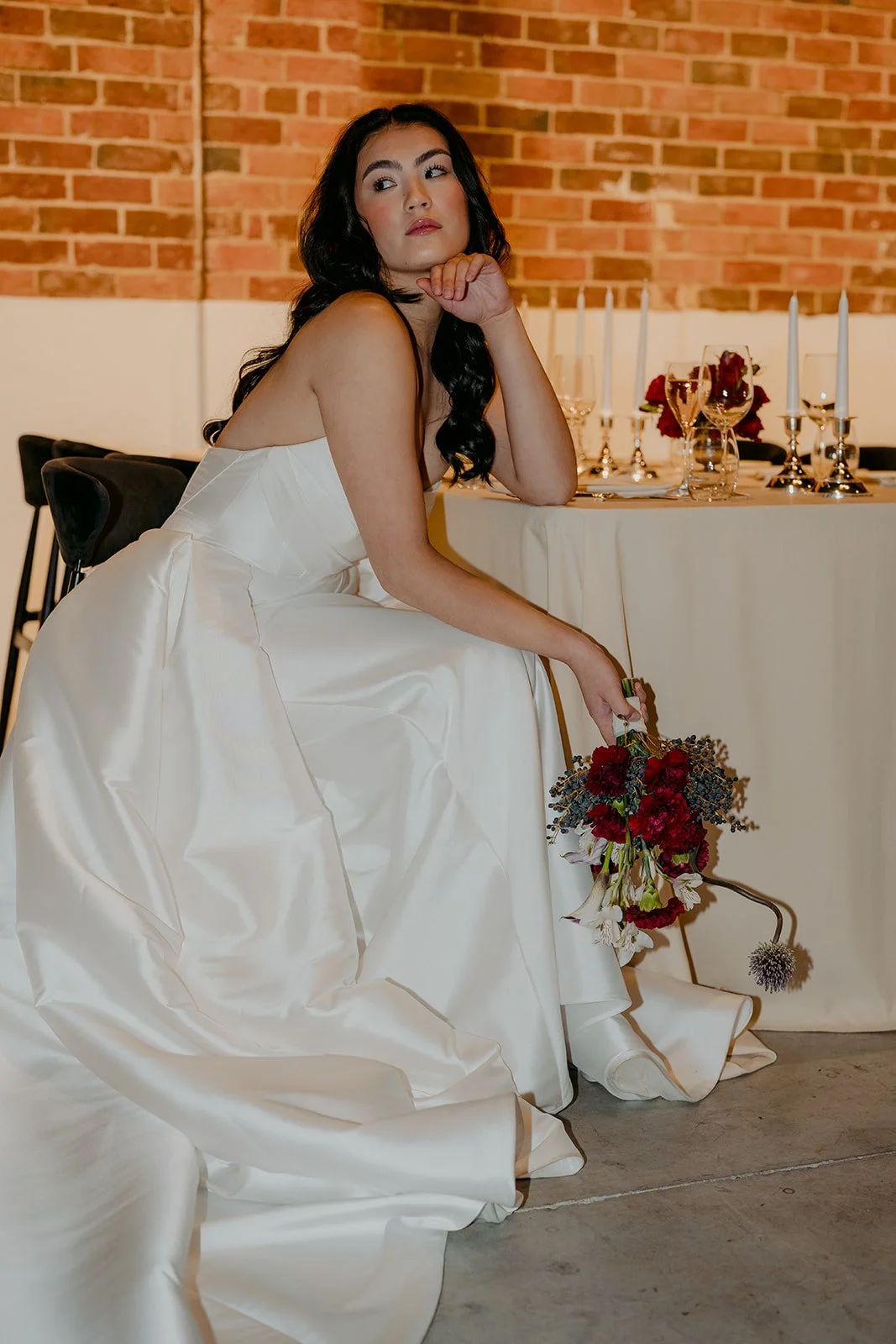 Bride seated at a rectangular banquet table at Nikola Estate wedding reception, featuring black velvet chairs and elegant table styling in the rustic Old Cellars venue.