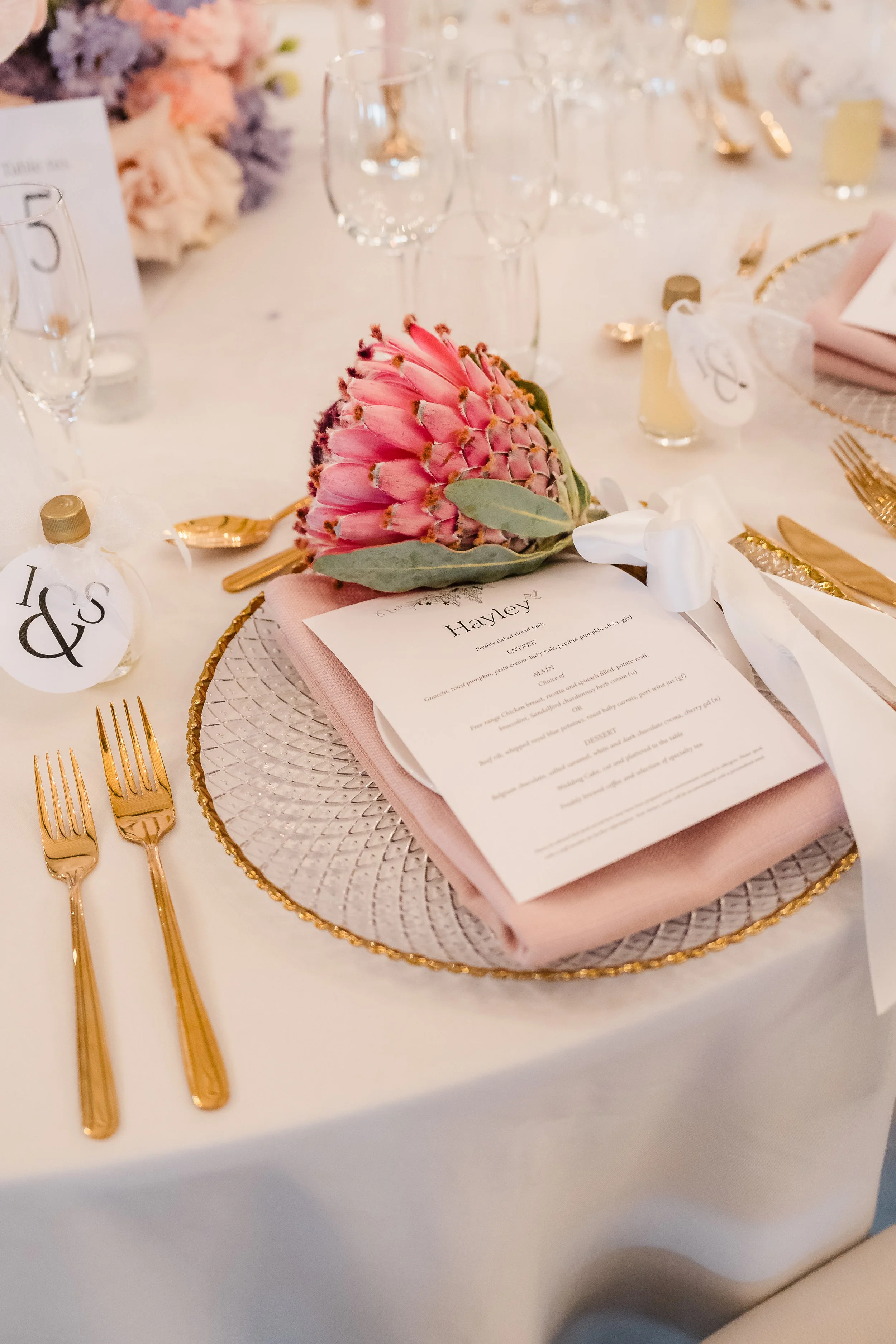 Gold-accented place setting with blush napkins and pink king protea, bespoke white menu