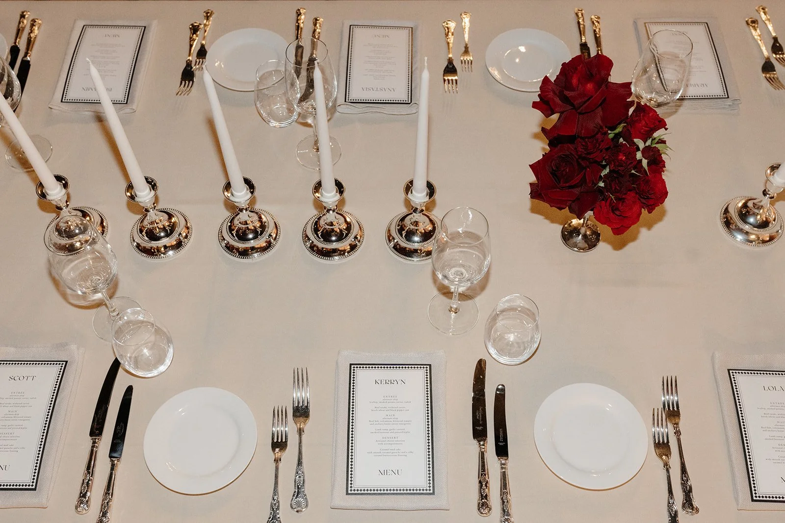 High-end wedding table styling at Nikola Estate with rectangular banquet table, elegant place settings with silver accents and structural red rose floral centrepiece, with tan-on-tan napkin and tablecloth.