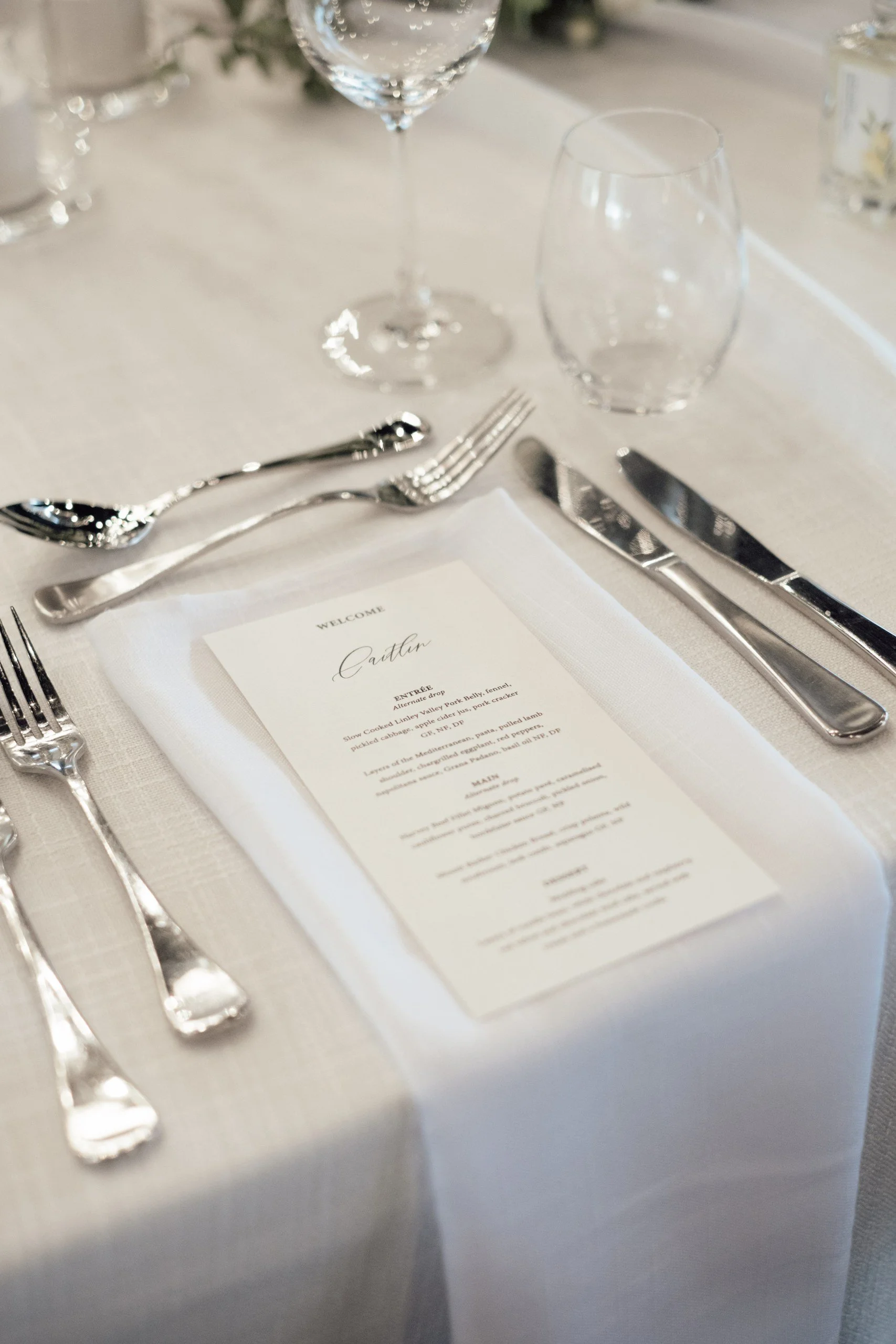 Wedding place setting with contemporary black and white menu design, white linens and refined tableware.