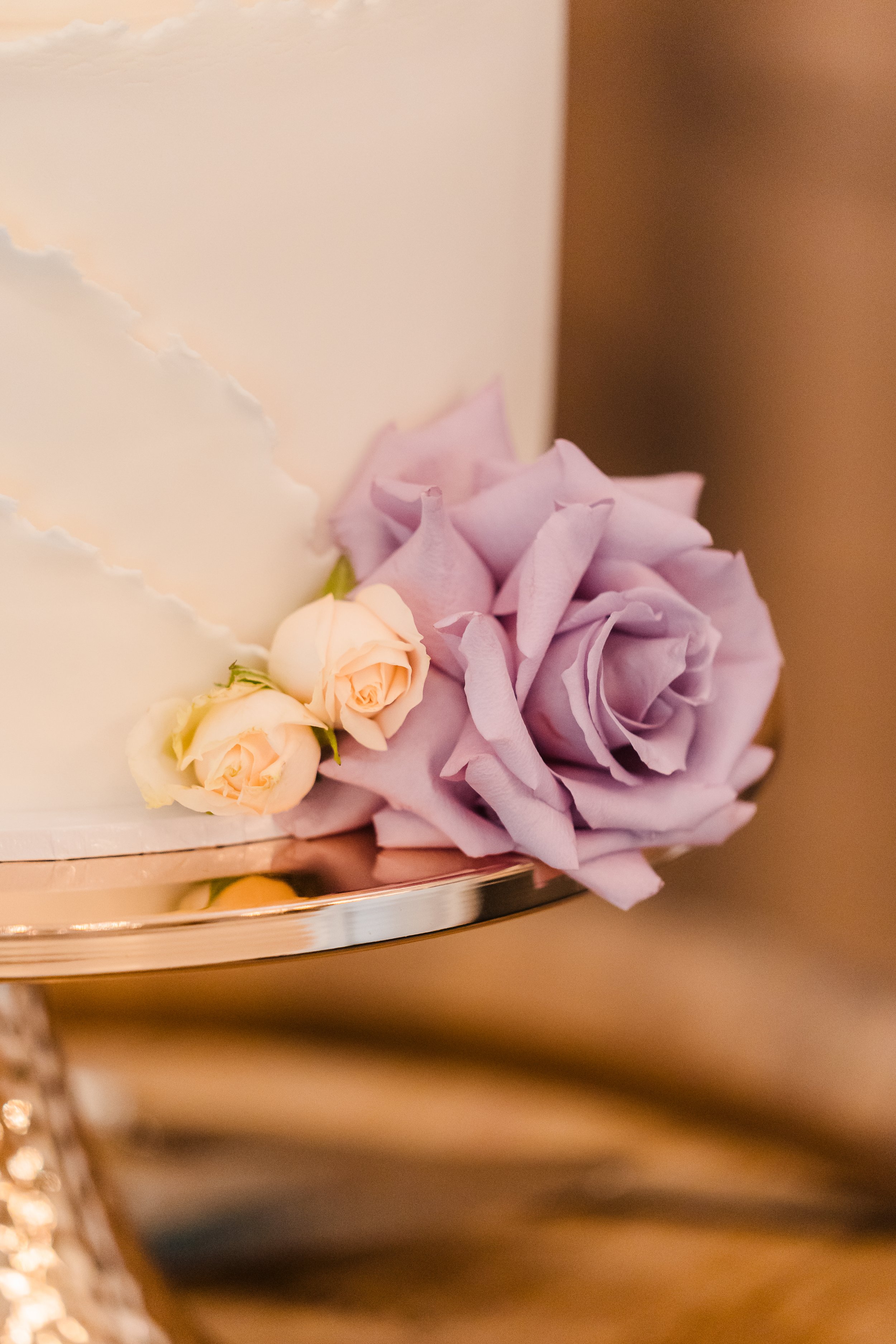 Light purple rose floral accent on bottom tier of three-tier white wedding cake