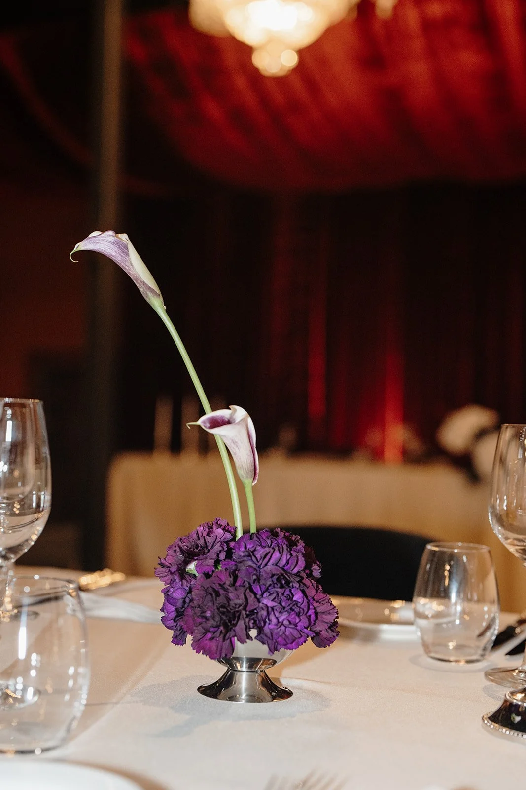 Warm ambient lighting highlighting the bold, luxurious design of a Nikola Estate wedding reception, including velvet seating, dramatic draping, and statement florals in a historic brick venue.