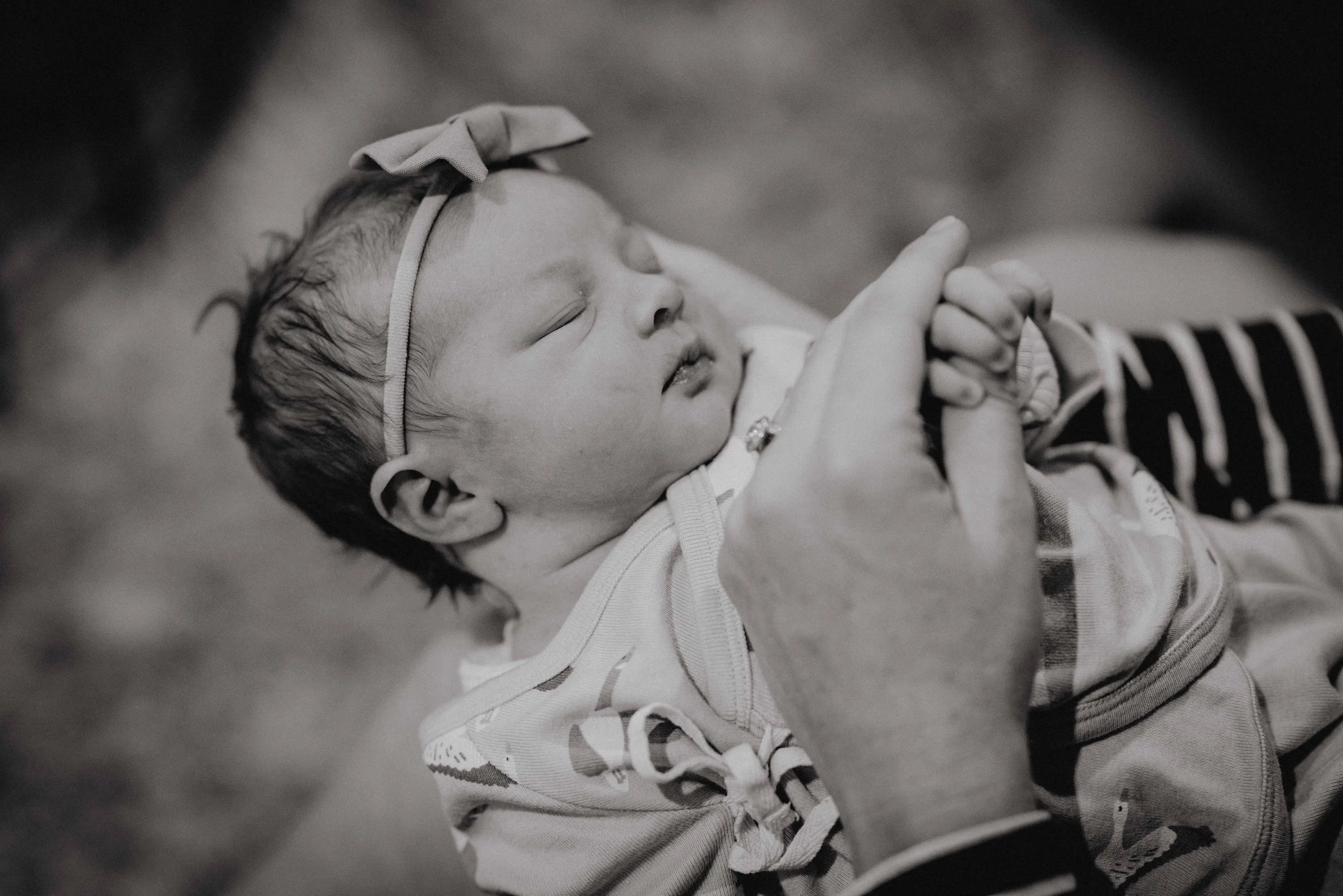 A sleeping baby with a headband held gently by an adult's hand, in black and white.