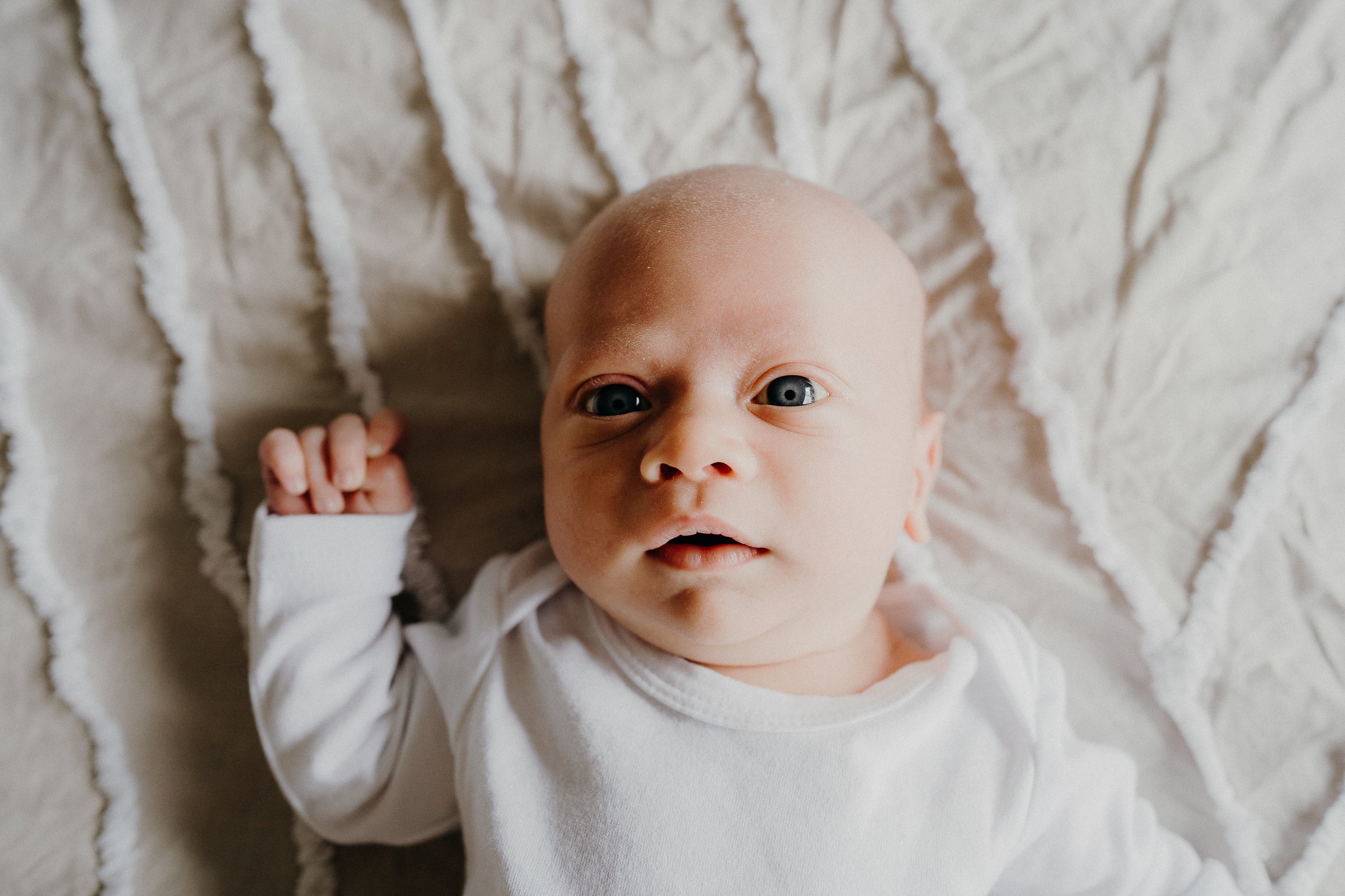 Newborn baby wearing a white onesie lying on a textured blanket