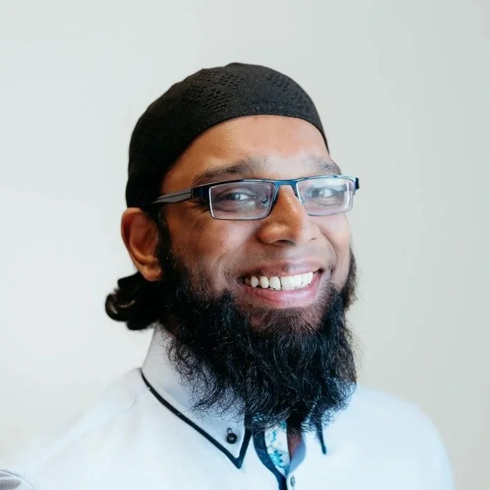 A man with a beard wearing glasses and a black cap, smiling and looking at the camera.