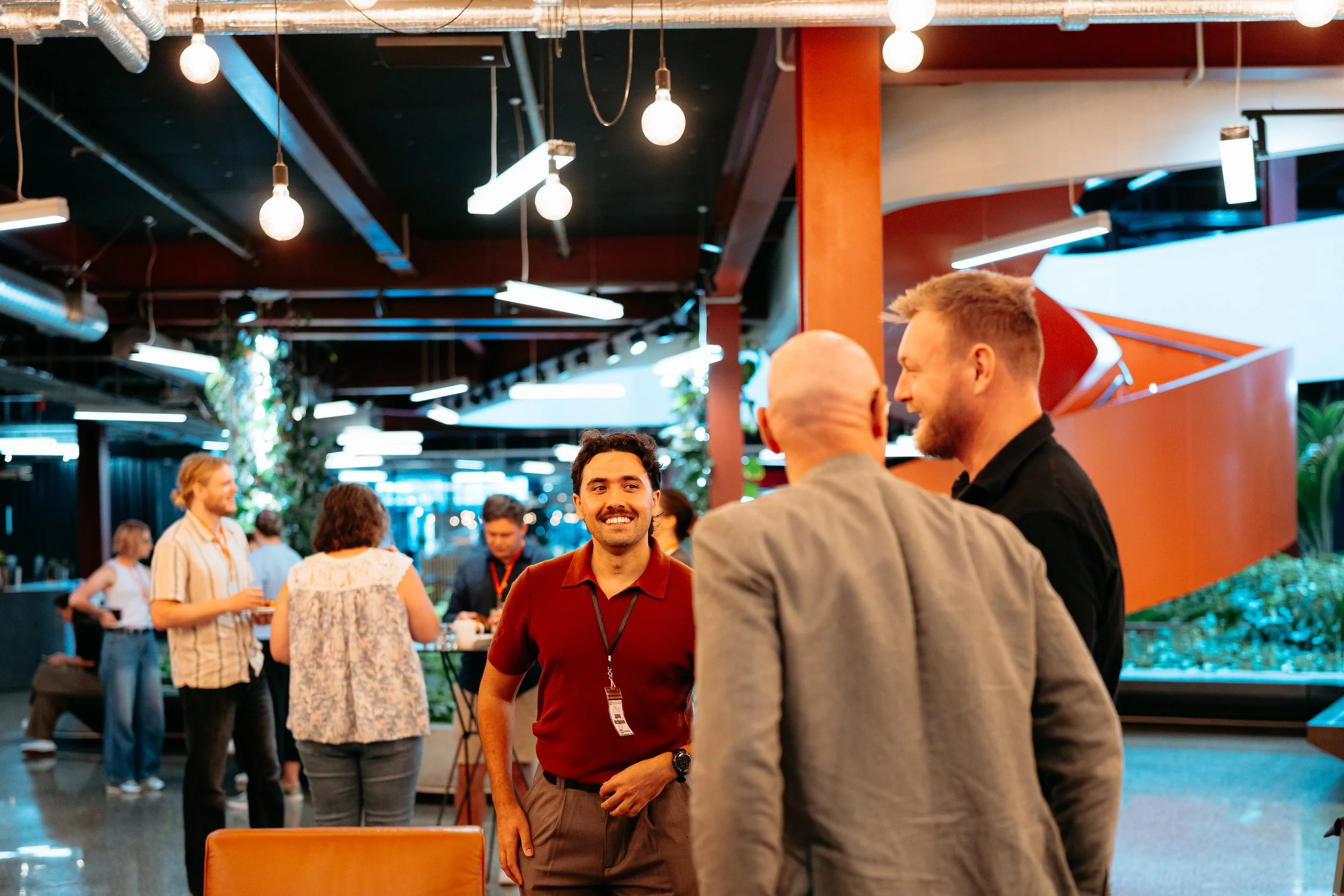 People socializing in an indoor setting with modern lighting and decor, including a man smiling at others in foreground.