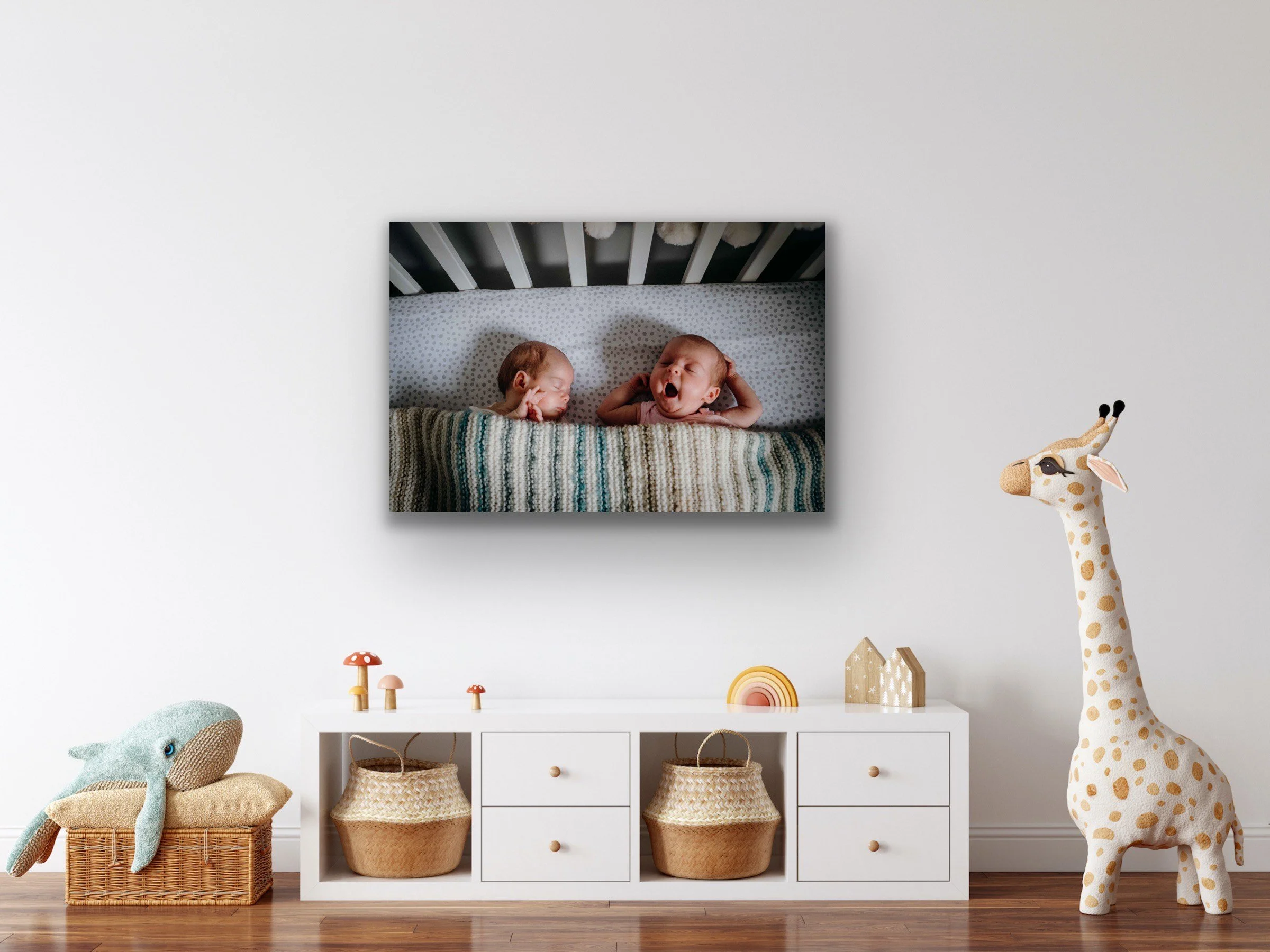 Nursery room with photo of two babies on the wall, toy giraffe, wooden cabinet, and wicker basket.