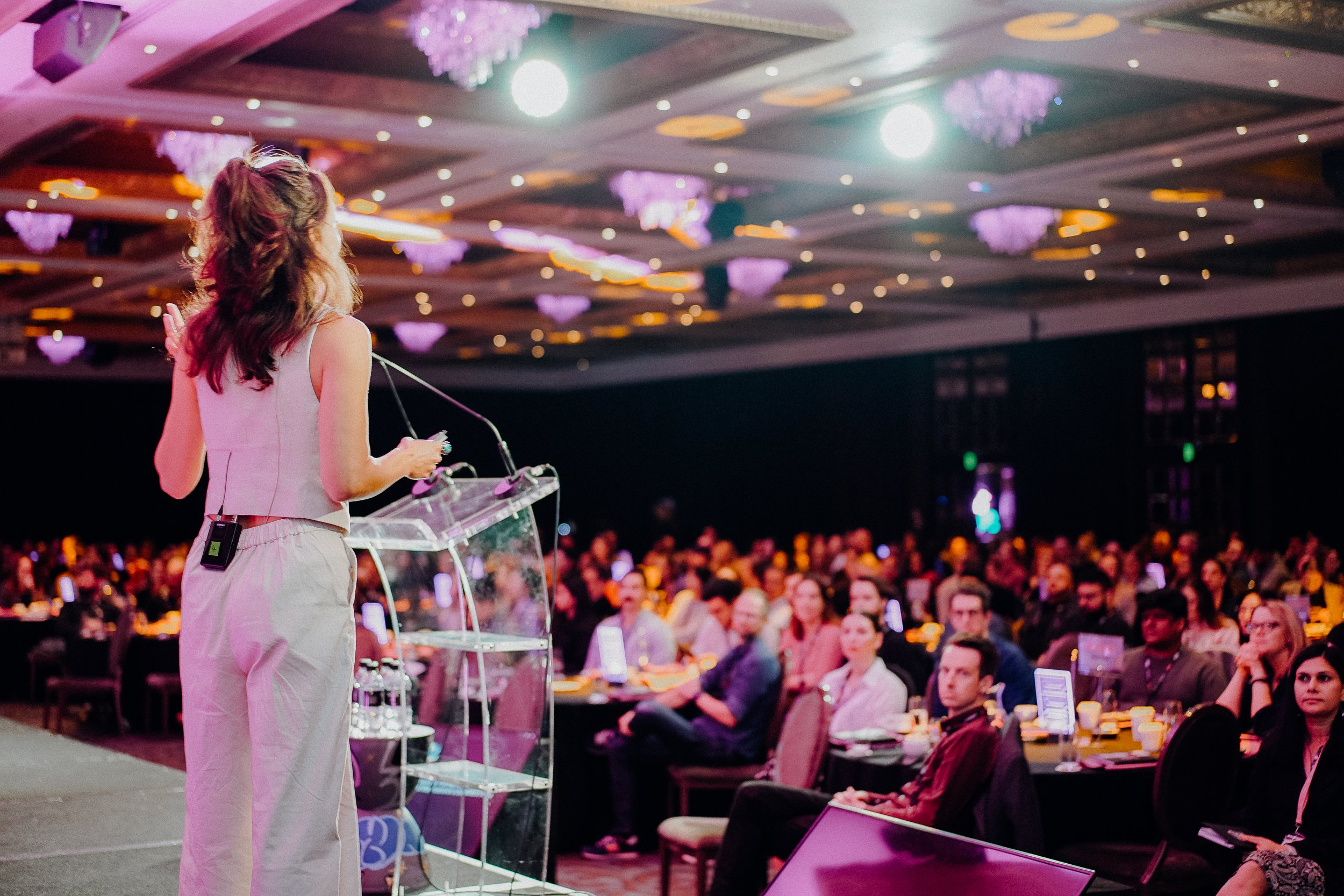 Woman speaking at a podium to an audience in a conference setting.