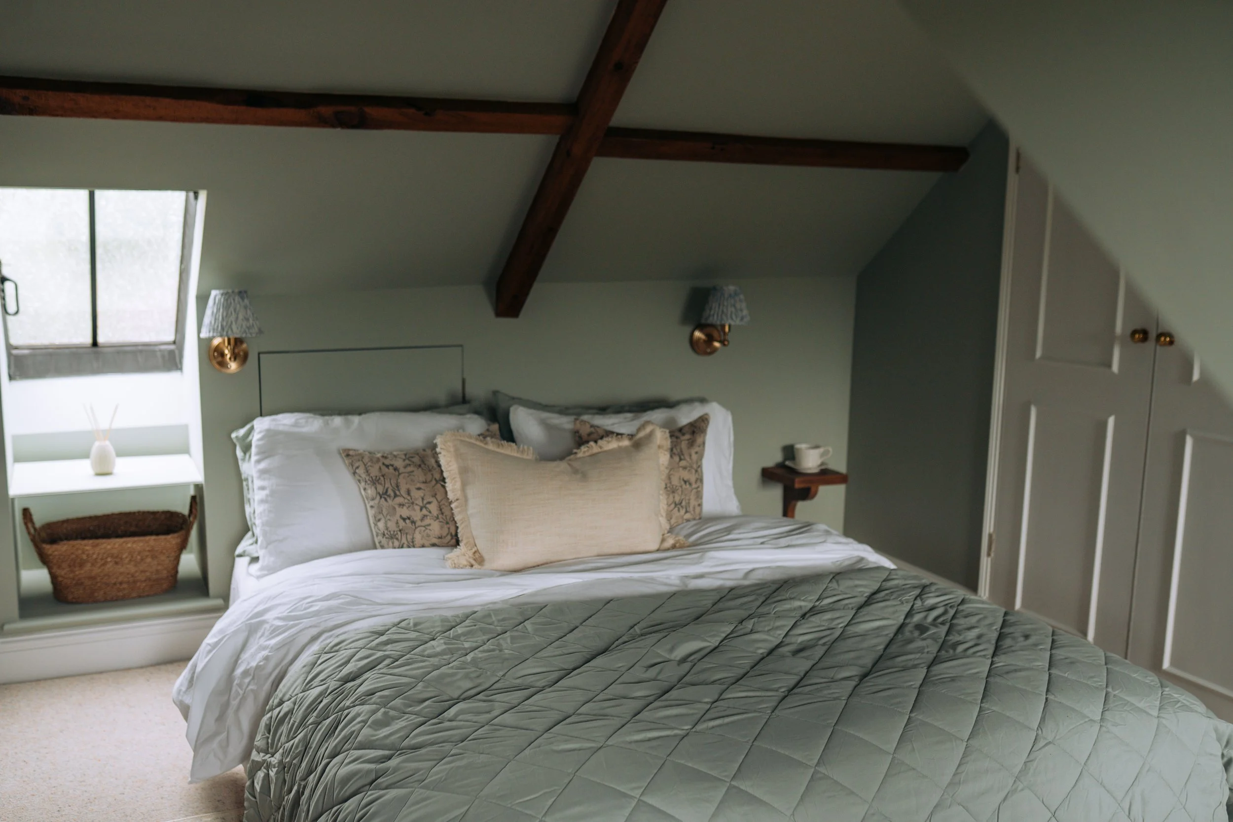 Sage green attic bedroom with beams at Moon End Cottage, Somerset