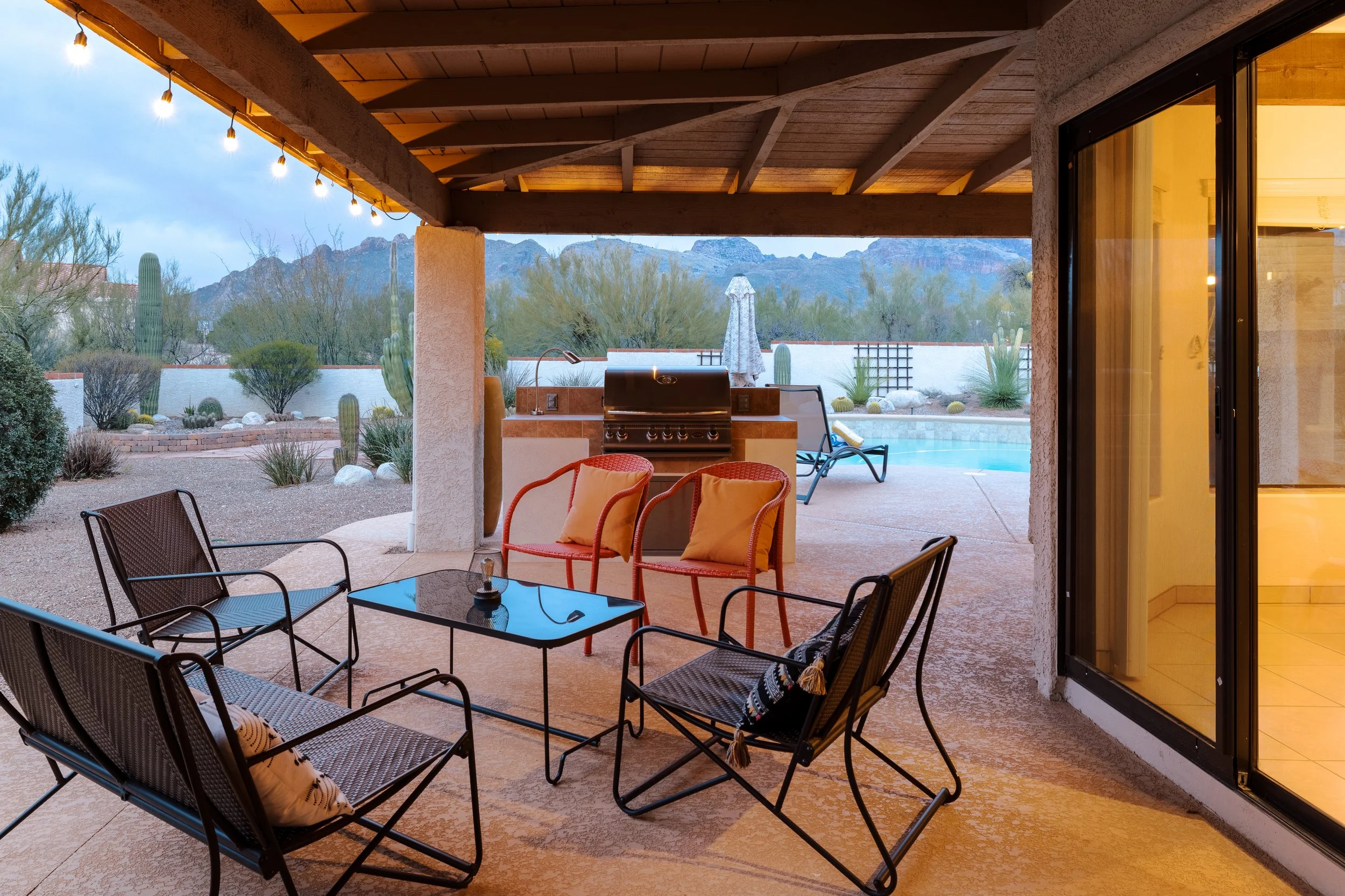 Covered patio with outdoor seating, dining table, built-in grill, and views of the Catalina Mountains beyond the backyard.