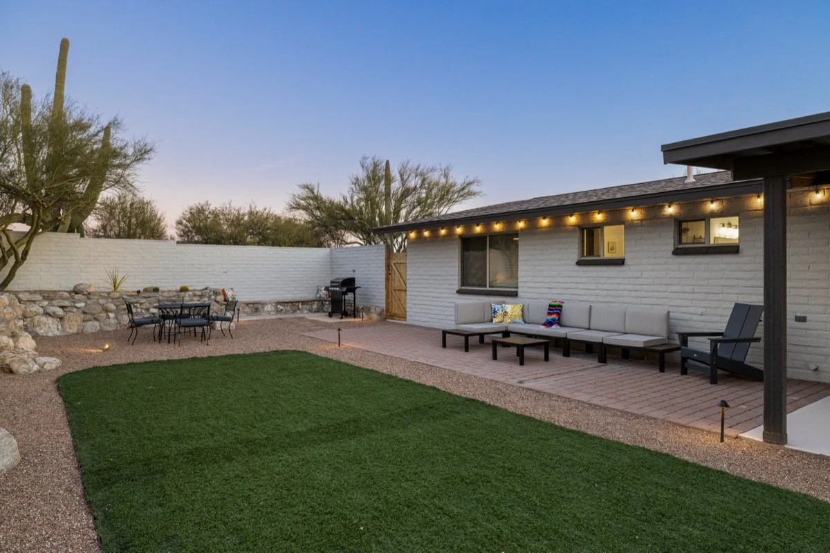 Private backyard with a grassy lawn, patio seating, string lights, and outdoor dining space for relaxing or gathering outdoors.