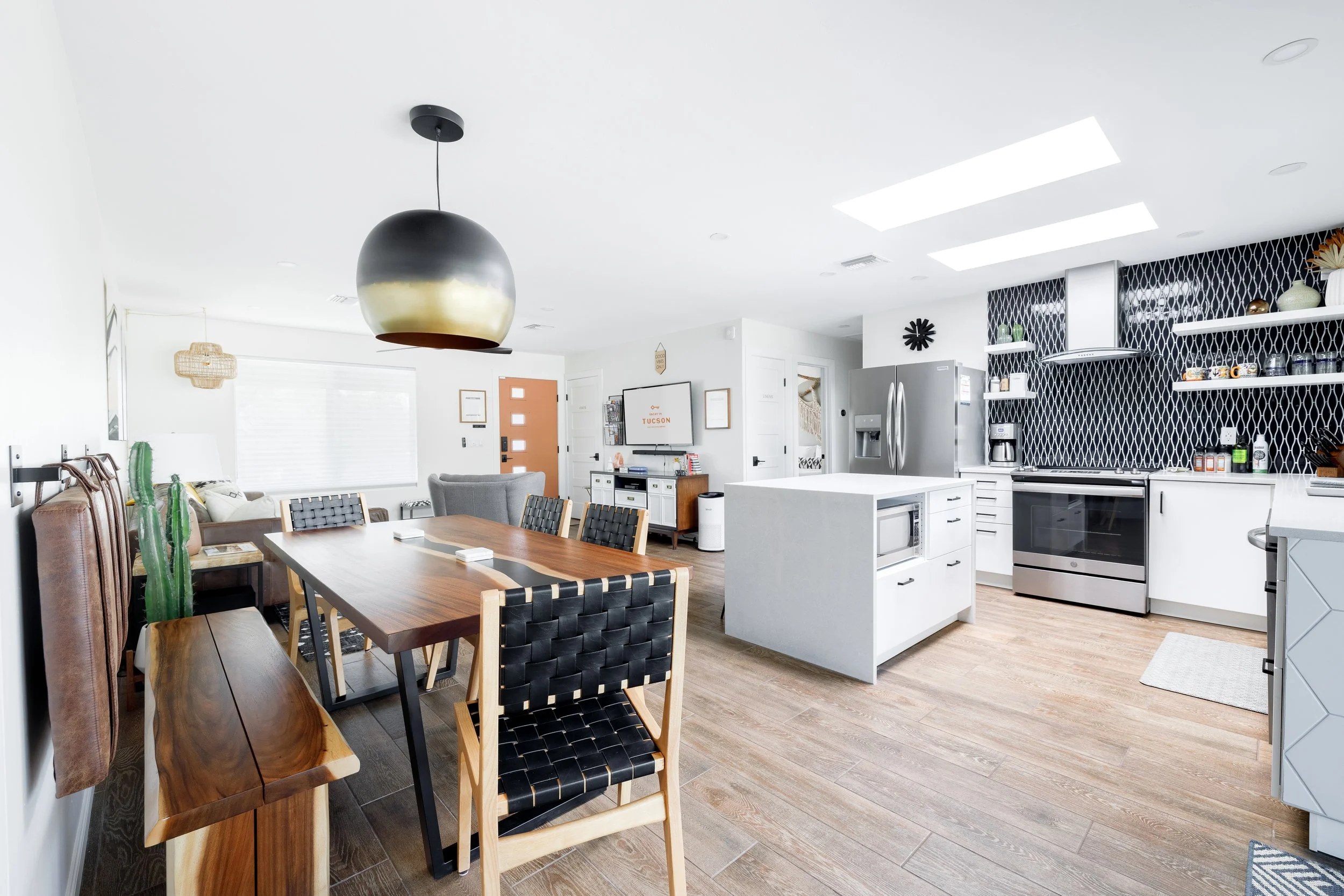 Bright open kitchen and dining area at Casa Palma with a wood dining table, black woven chairs, white cabinetry, stainless-steel appliances, modern pendant lights, and a black patterned backsplash.