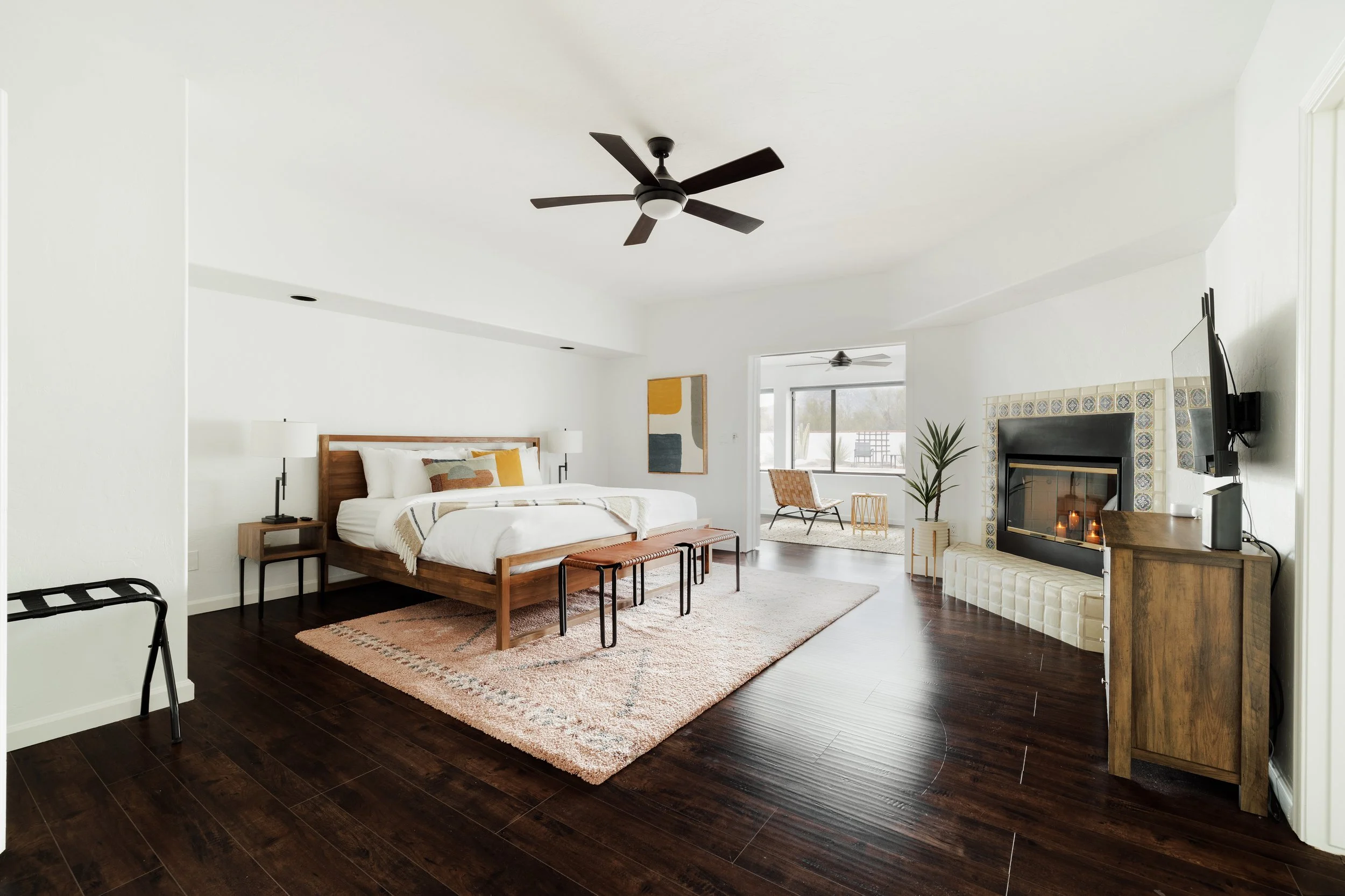 Primary bedroom with a king bed, dark wood floors, and light from the attached Arizona room with view of the Catalina Mountains in the distance.