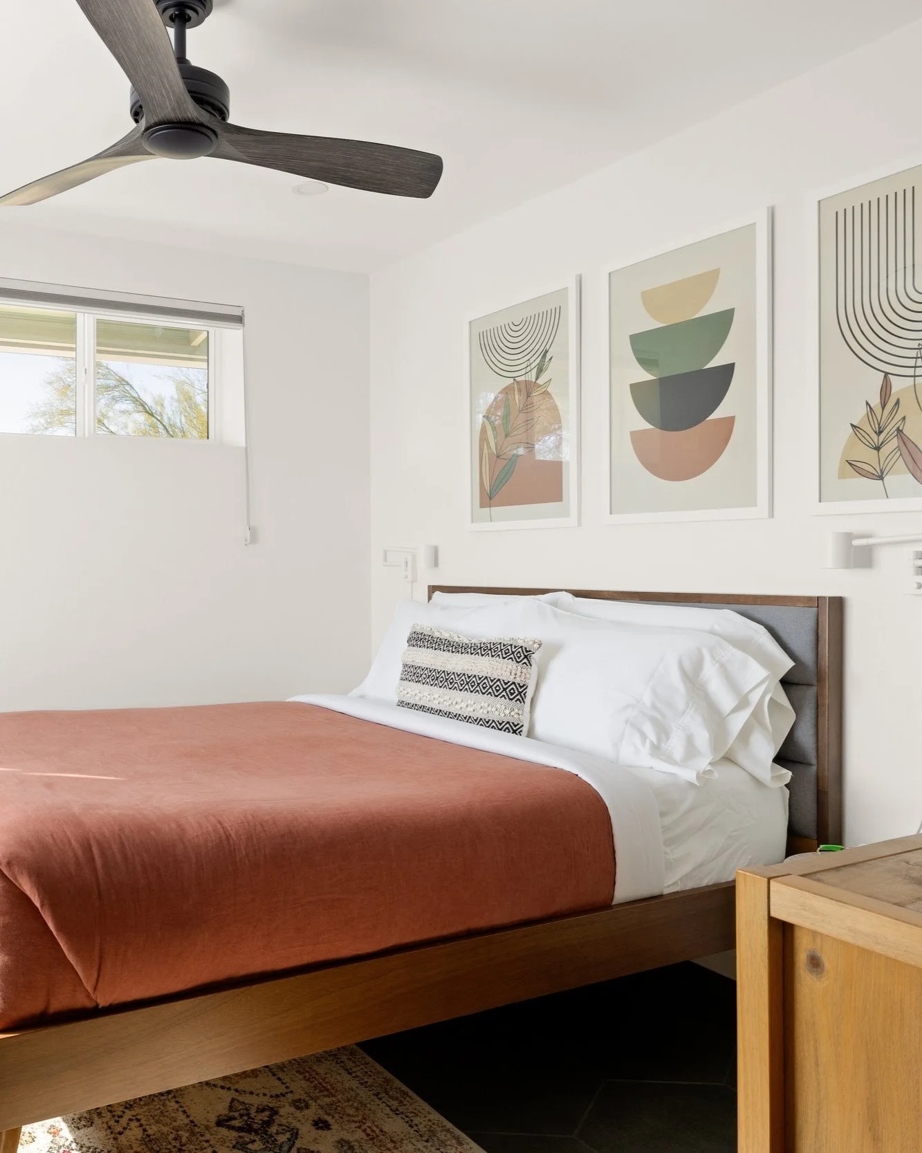 A warm wood bed with rust-colored bedding sits beneath two framed geometrical prints.