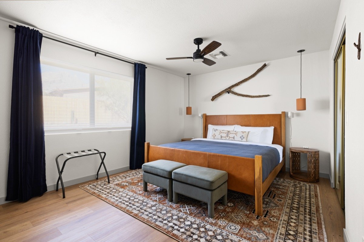Wood and leather bed with blue bedding beneath natural cholla branch wall art, flanked by terracotta colored pendant lights and dark blue curtains.