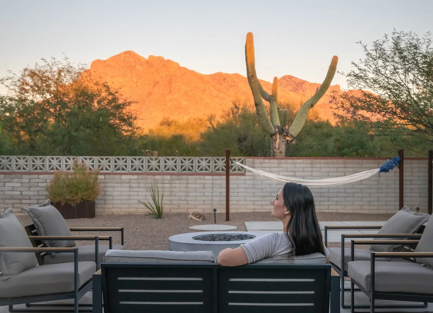 Woman sitting in the backyard at Casa Palma vacation rental looking at the desert landscape with a saguaro and Catalina mountains.