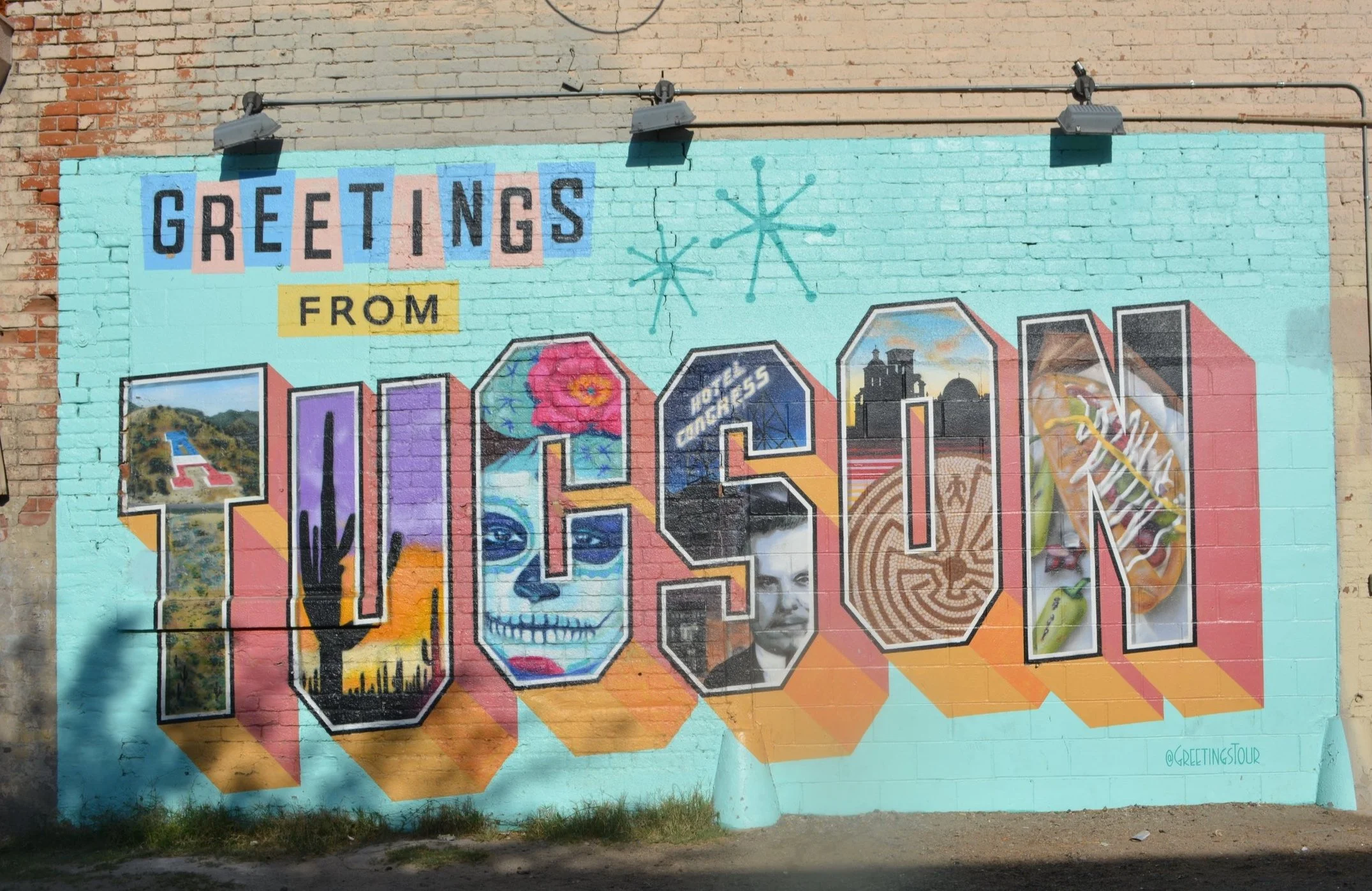 Turquoise postcard-style mural reading Greetings From Tucson, with colorful local landmarks and desert imagery filling the oversized letters.