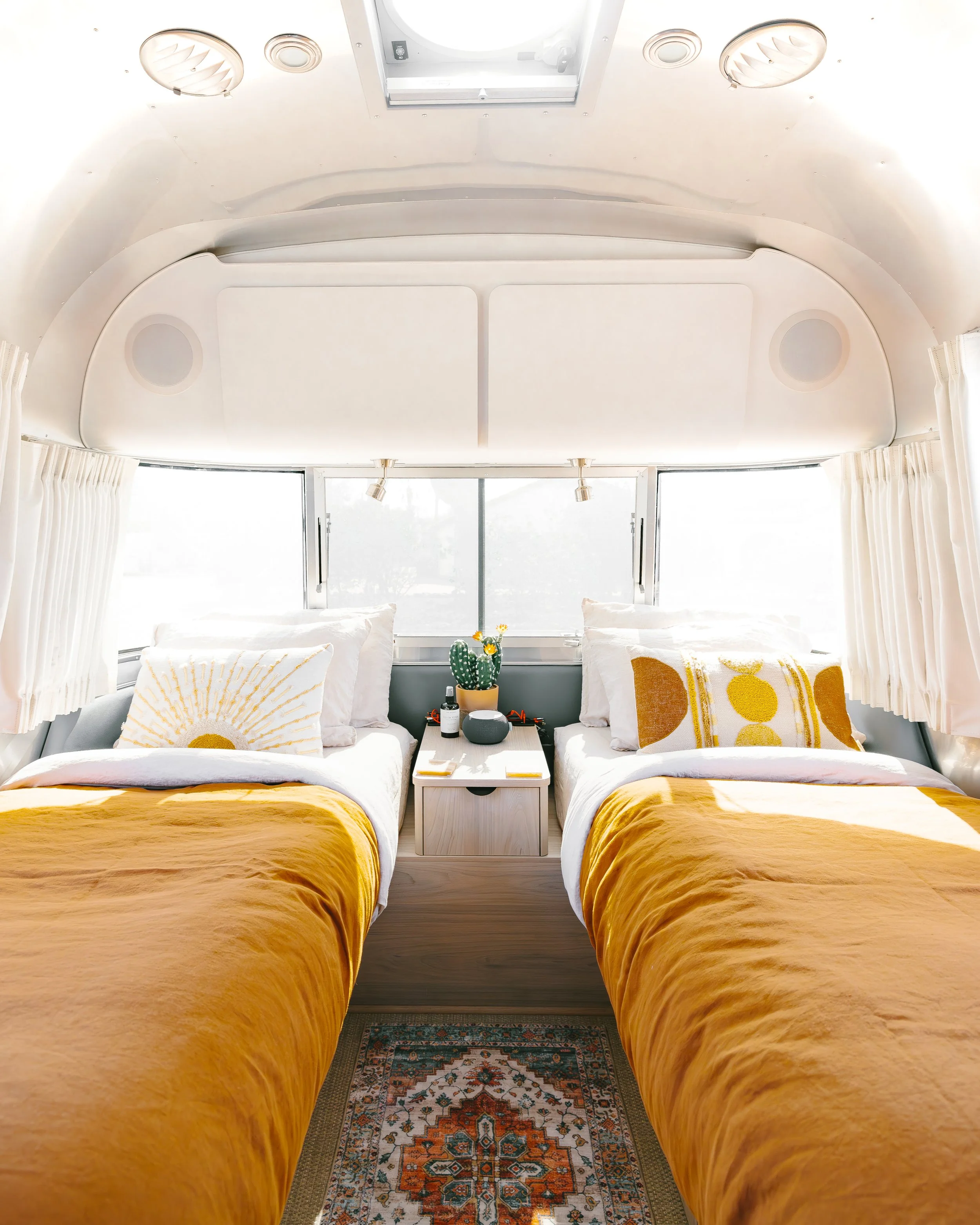Bedroom with two xl twin beds, mustard-colored blankets, a shared nightstand, and windows surrounding the sleeping area.