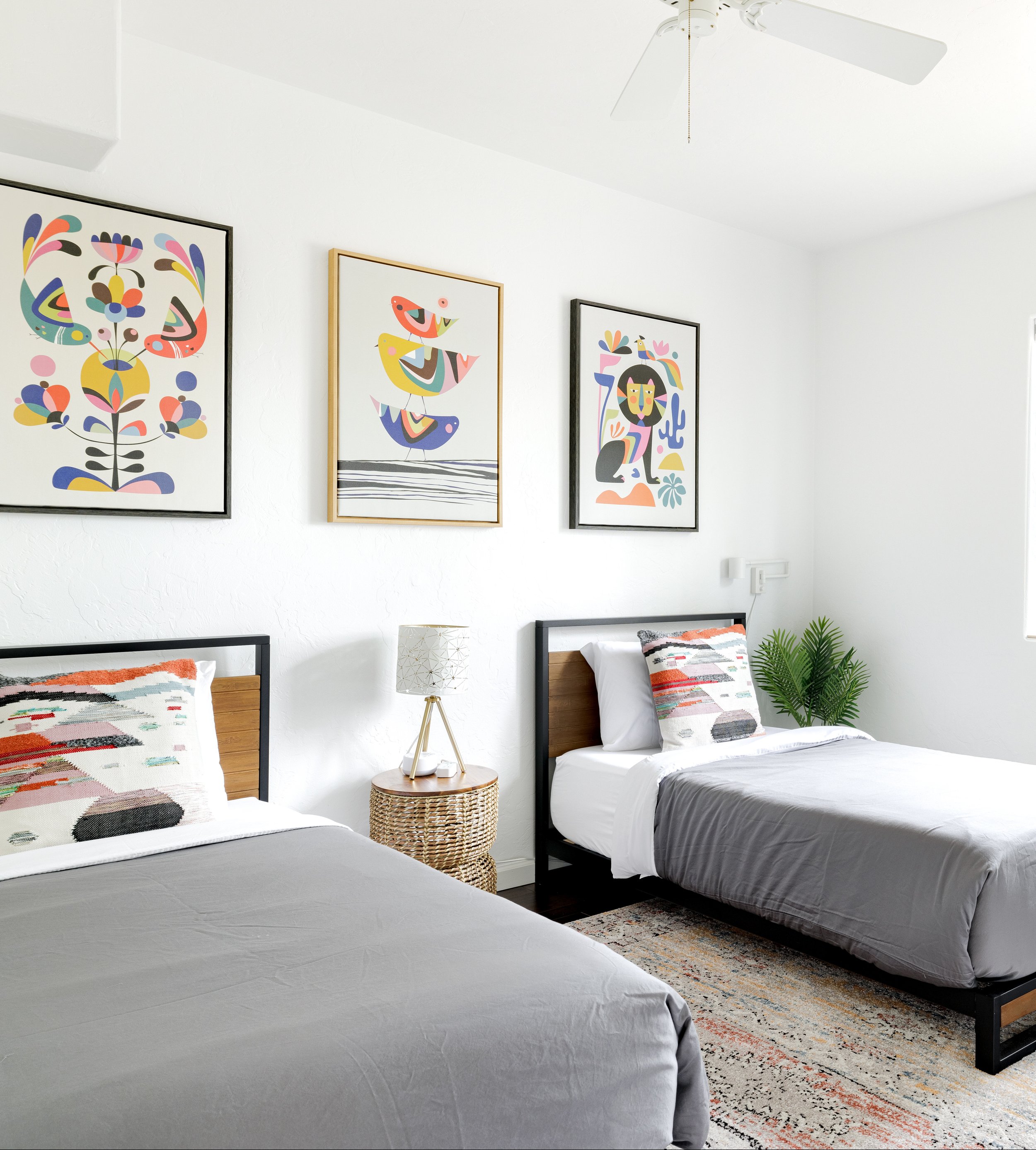 Bedroom with two twin beds, colorful framed artwork, a shared bedside table, and a patterned area rug.