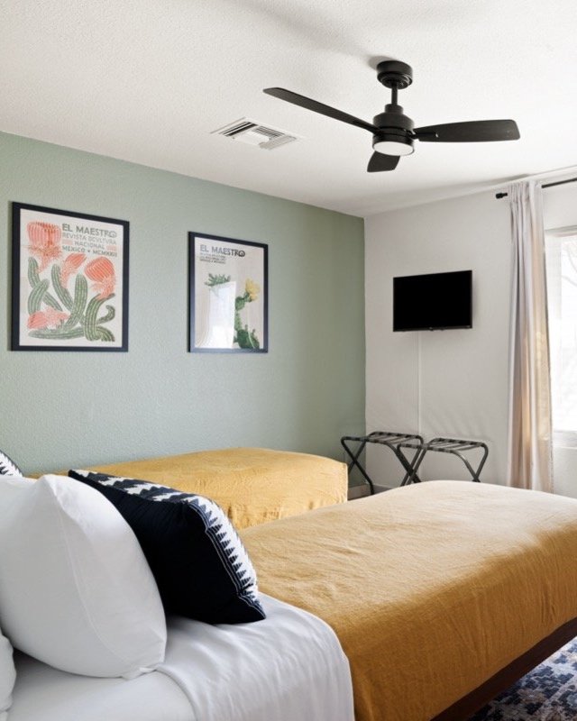 Bedroom with two Twin XL beds, botanical artwork, wall-mounted television, and luggage rack for flexible sleeping arrangements.