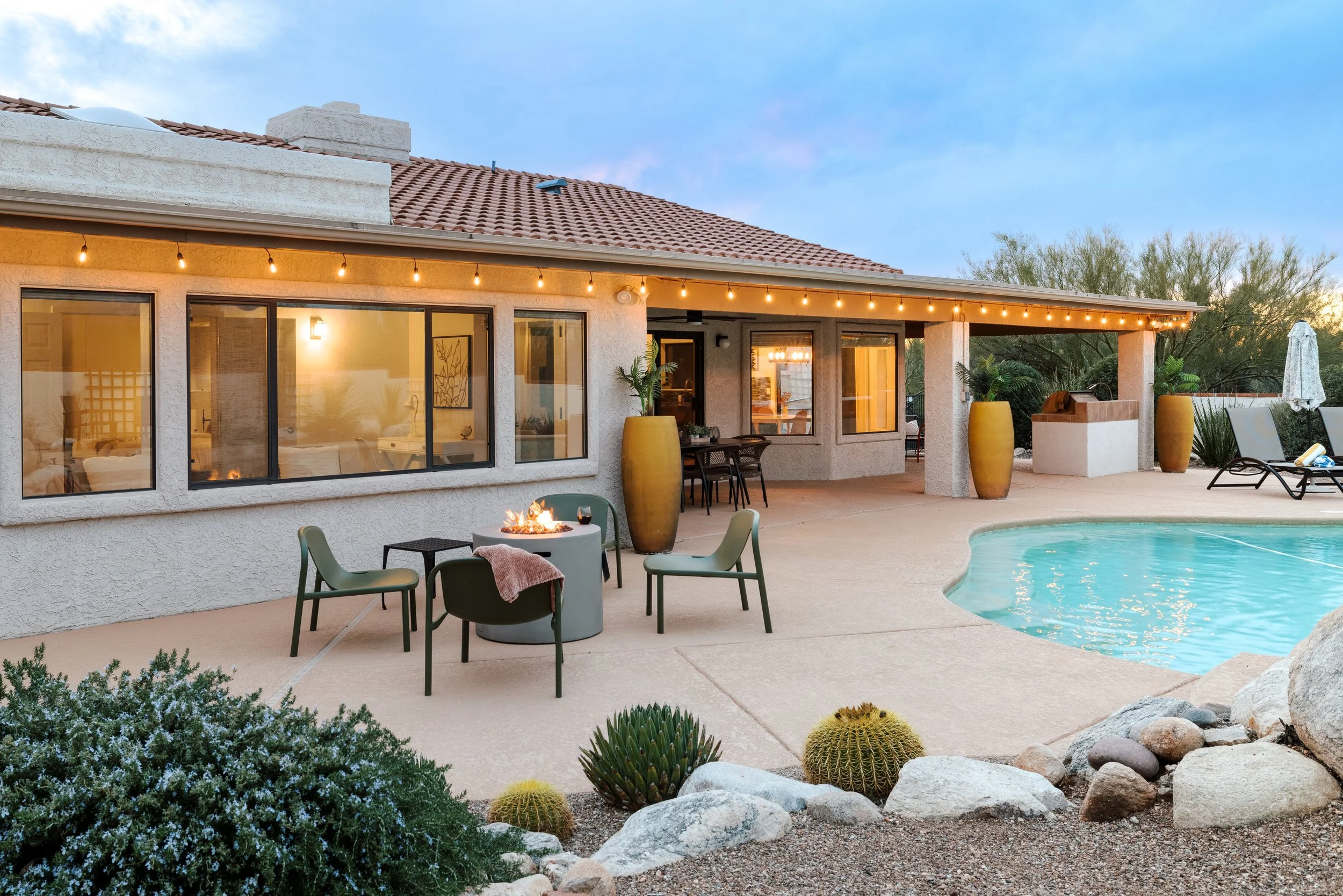 Backyard patio with glimpse of a swimming pool, fire pit seating, outdoor dining area, and sliding glass doors connecting to the home.
