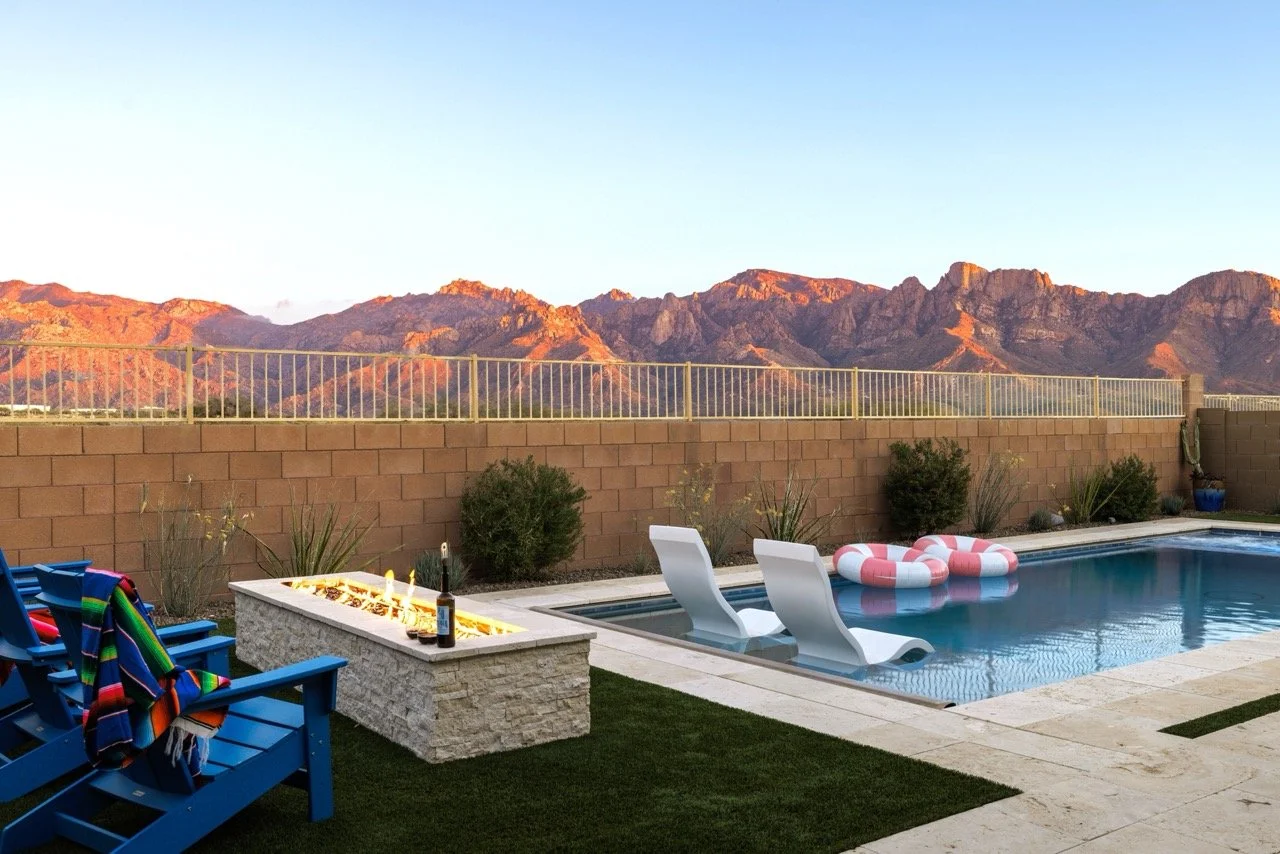 Pool with in-water loungers, fire feature, and panoramic Catalina Mountain views at golden hour.