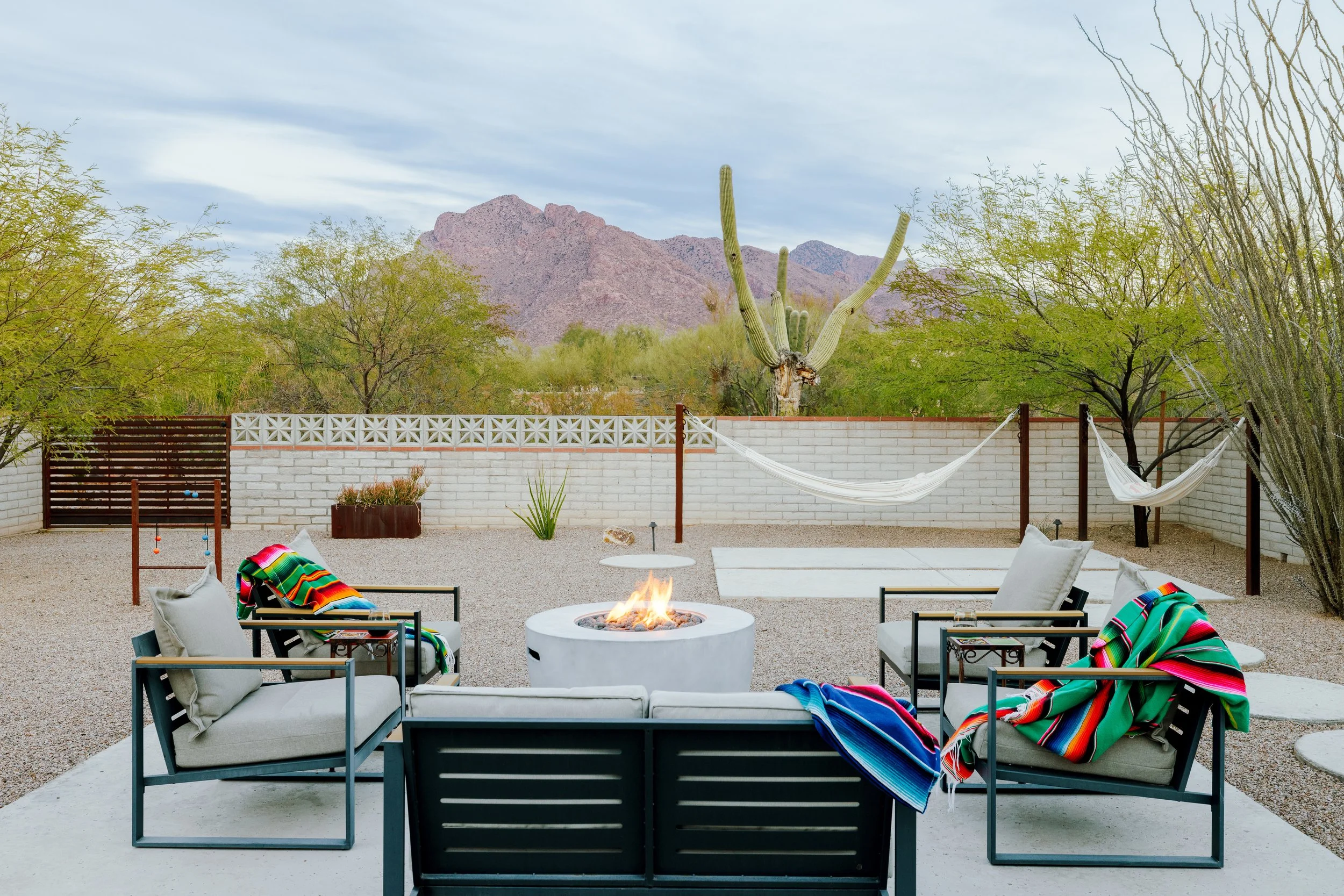 Backyard with a fire table, outdoor seating, hammock, saguaro cactus, and mountain views beyond the wall.