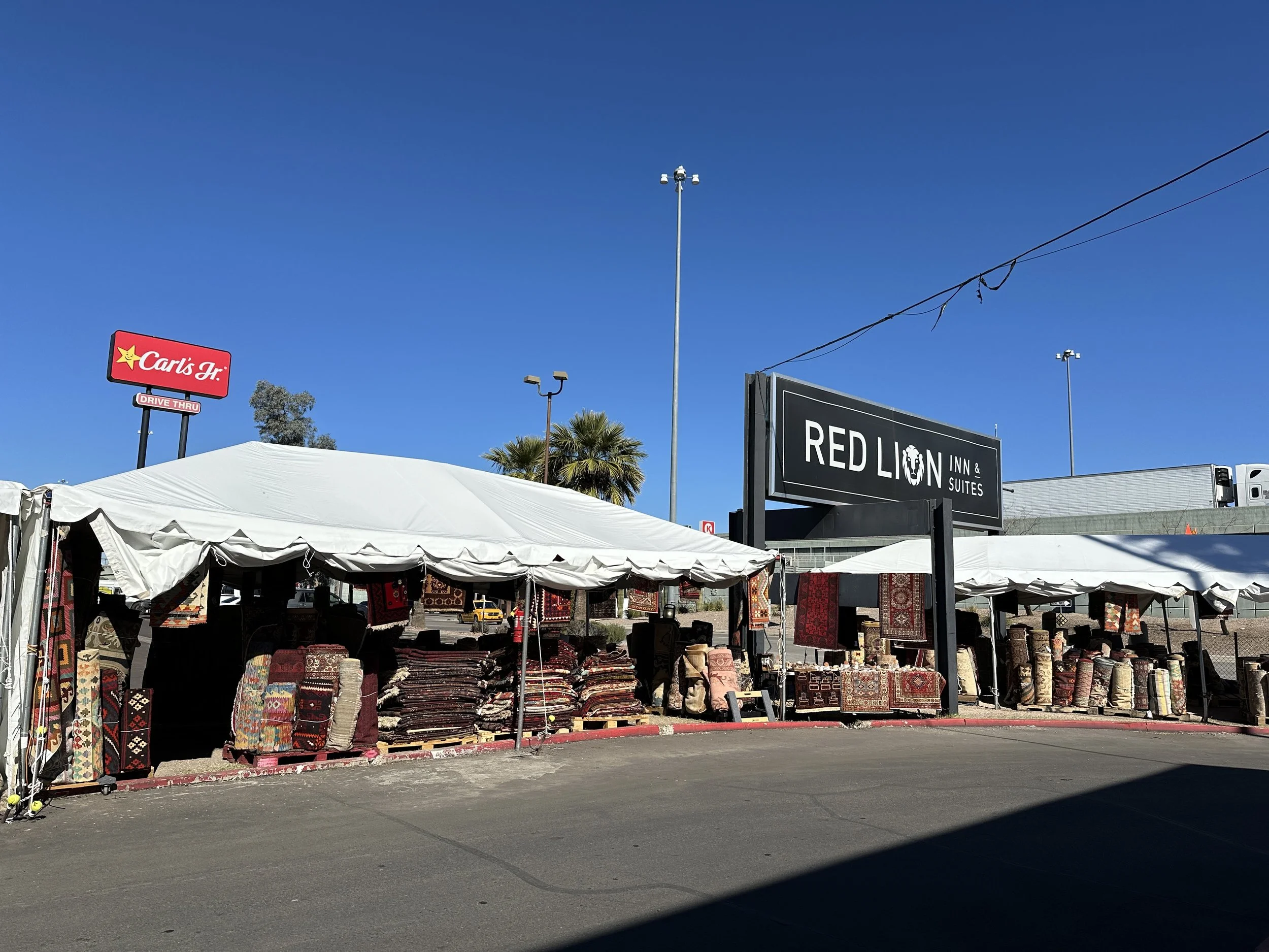 Outdoor vendor tents filled with stacks and hanging displays of colorful patterned rugs beside the Red Lion Inn during the Tucson gem shows.