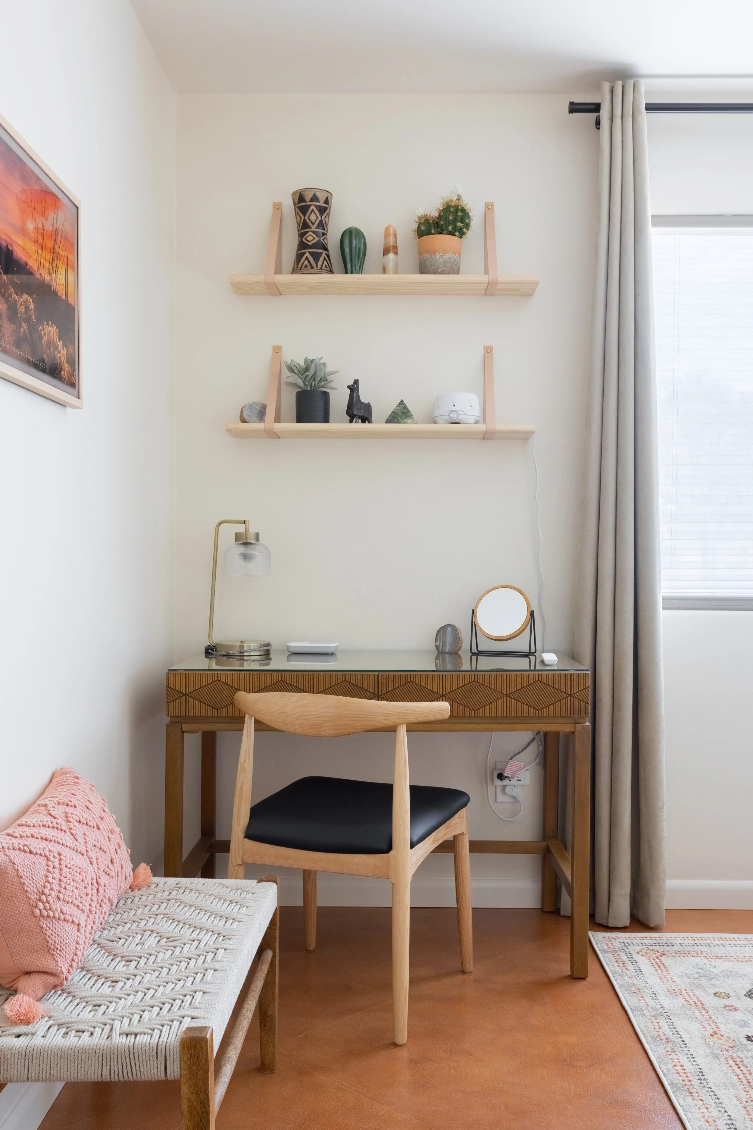 Wood writing desk with a brass lamp and chair beneath two floating shelves displaying desert-inspired décor and potted plants.