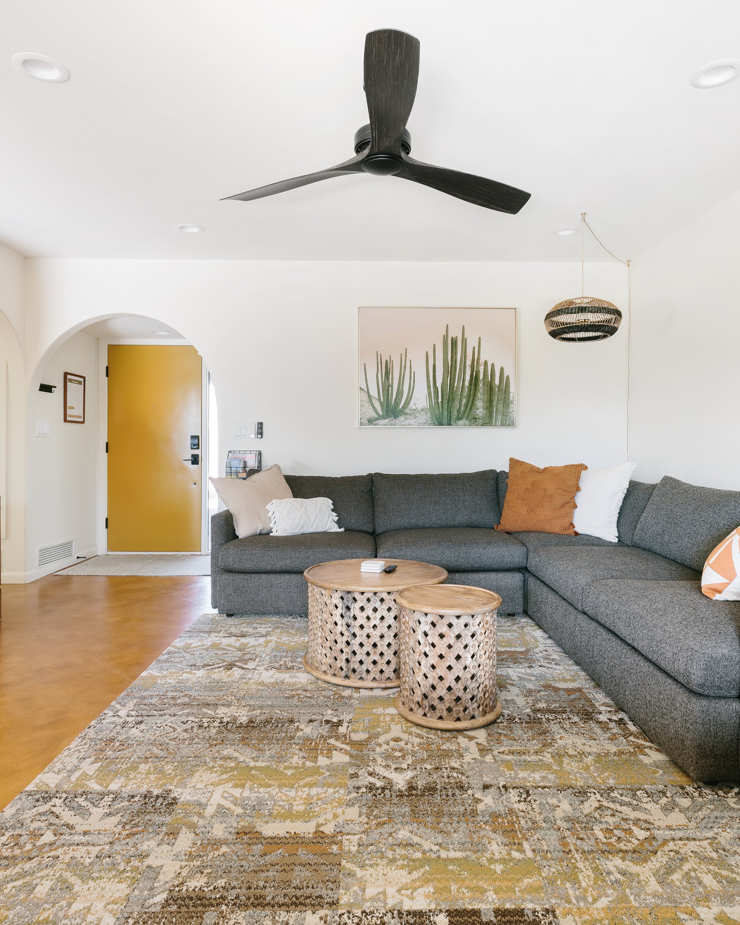 Living room with a large sectional sofa, two round coffee tables, area rug, ceiling fan, and cactus artwork on the wall.