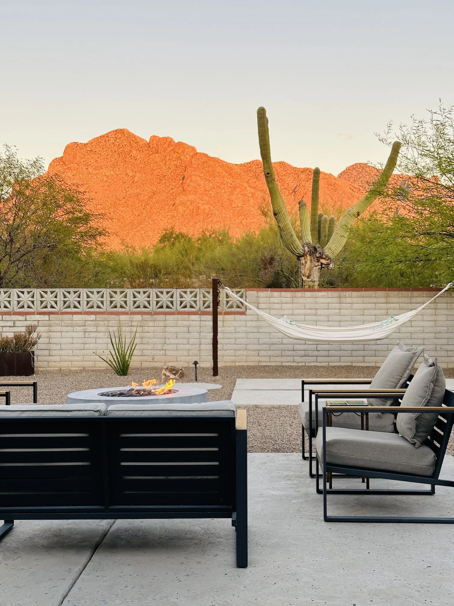 Backyard seating area with a fire table, hammock, and saguaro cactus overlooking sunlit Catalina Mountains.