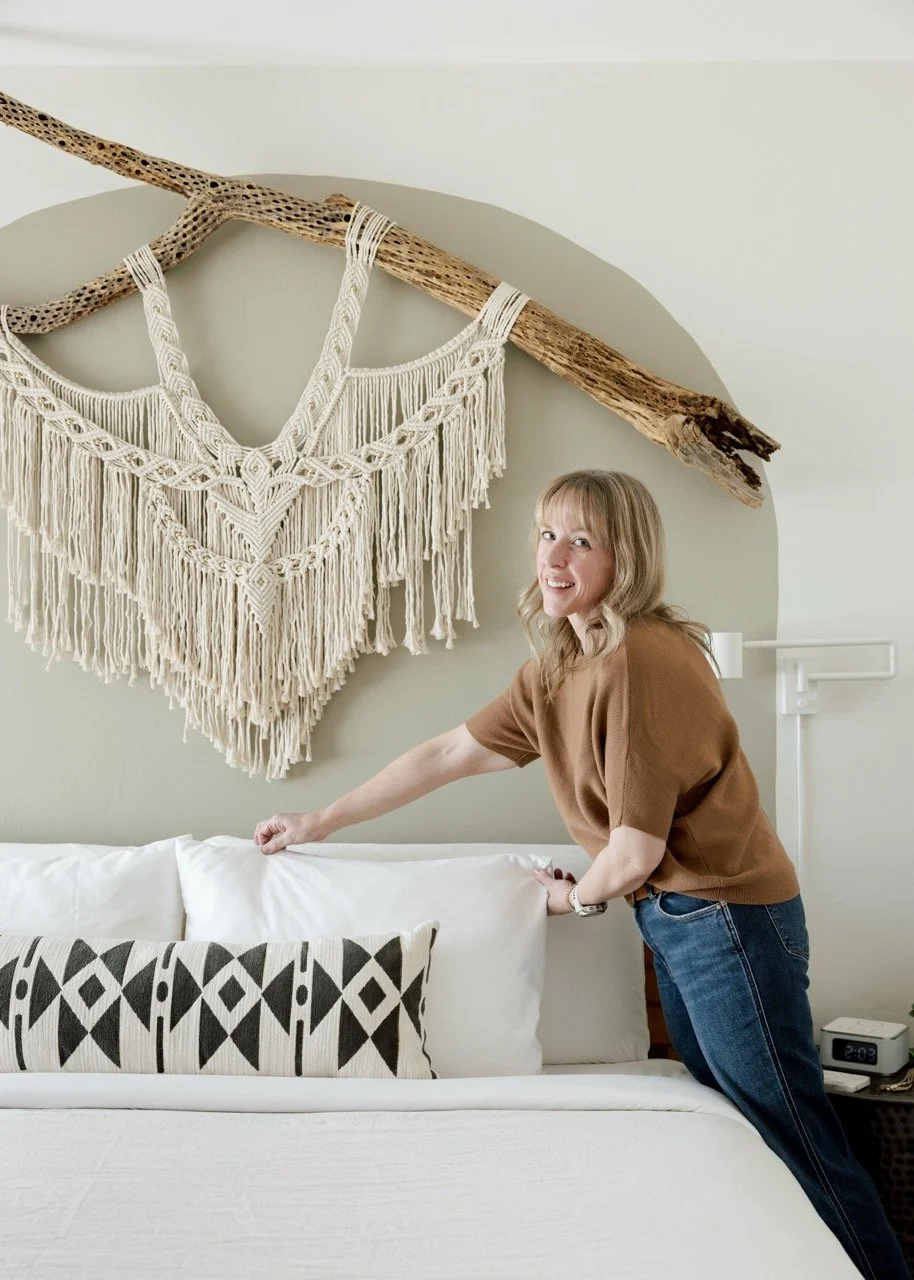 Vacay in Tucson host is fluffing a pillow and smiling. There is a cholla cactus macrame art on the wall.