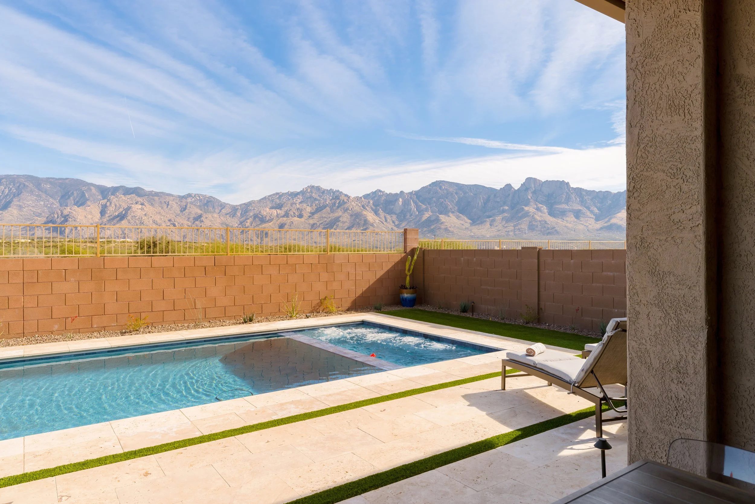 Clear backyard swimming pool and attached spa with a lounge chair on the patio and panoramic mountain views beyond a low block wall.