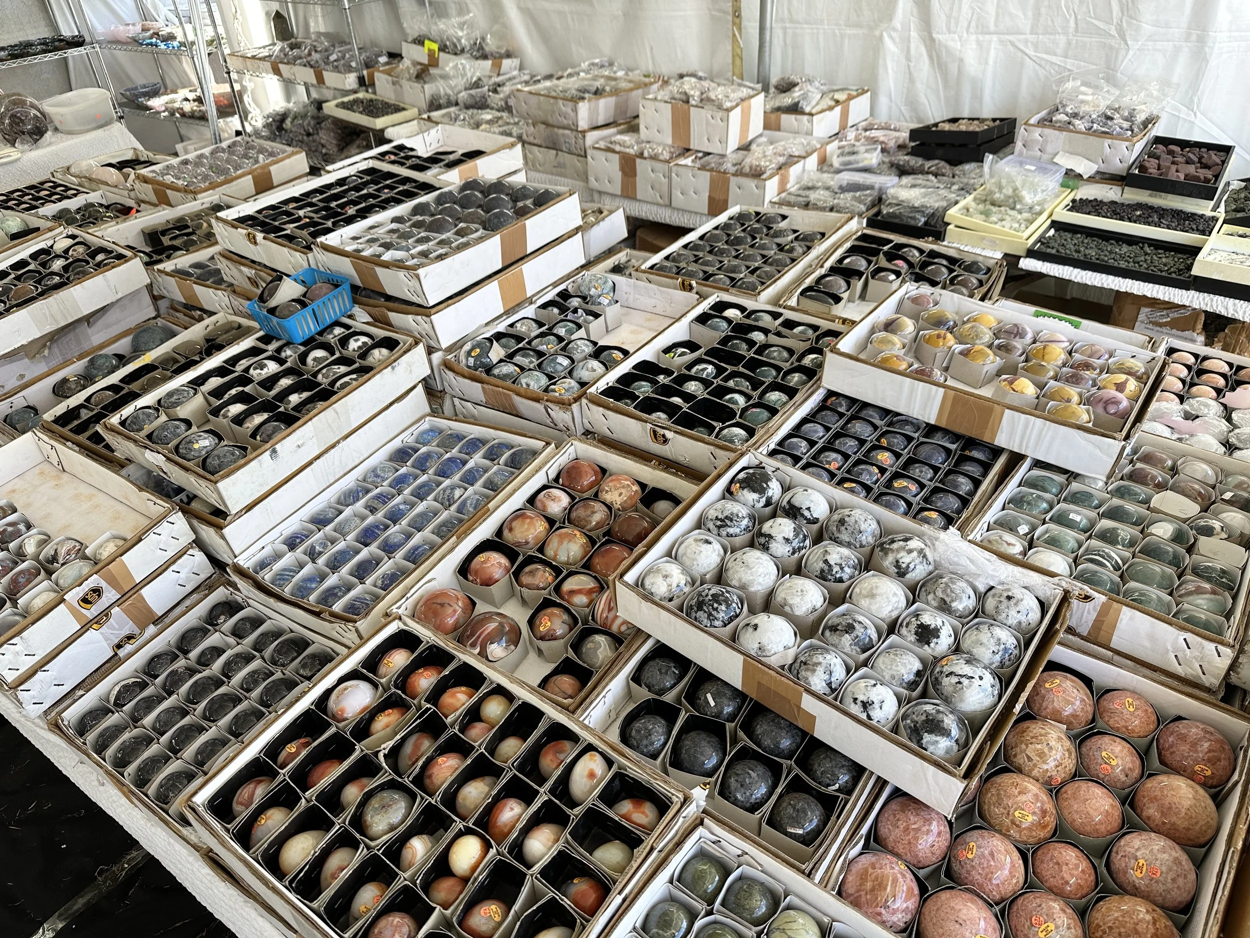 Open cardboard trays filled with polished stone spheres in many colors and patterns, arranged closely together on vendor tables.