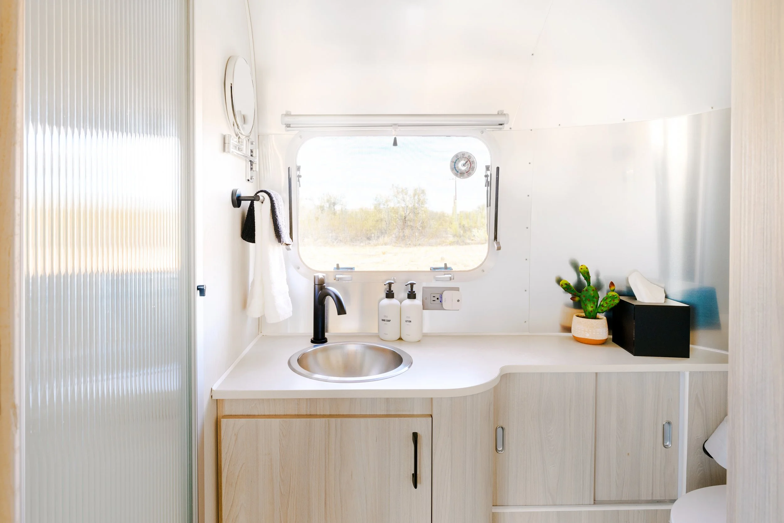 Compact bathroom with a small round sink, countertop, window, towel rack, and light wood cabinetry.