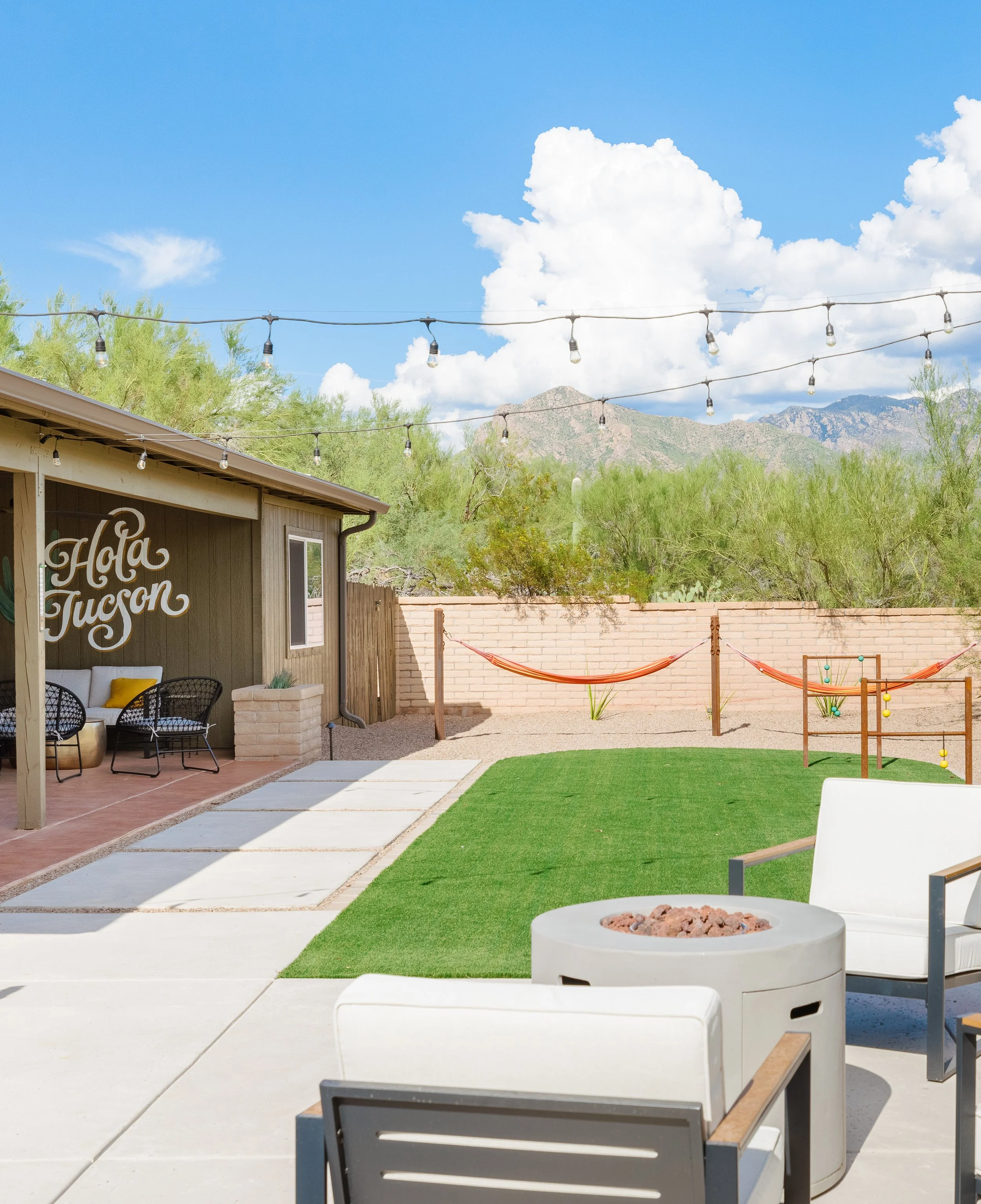 Backyard with artificial turf, hammocks, fire table, patio seating, string lights, and mountain views in the distance.