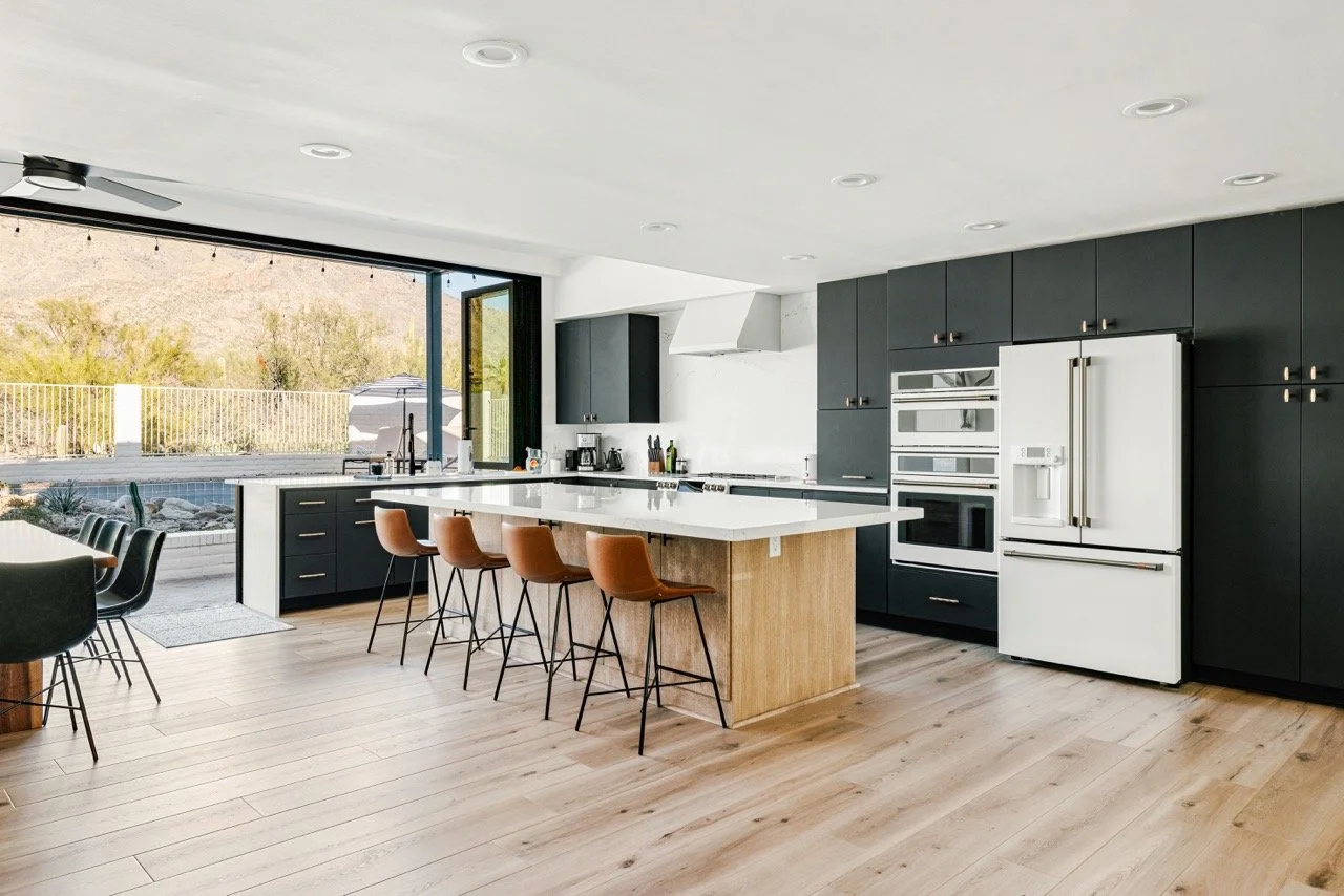 Modern chef's kitchen with a large island, bar seating for five, Café appliances, quartz countertops, and accordion doors opening toward the Catalina Foothills in Tucson.