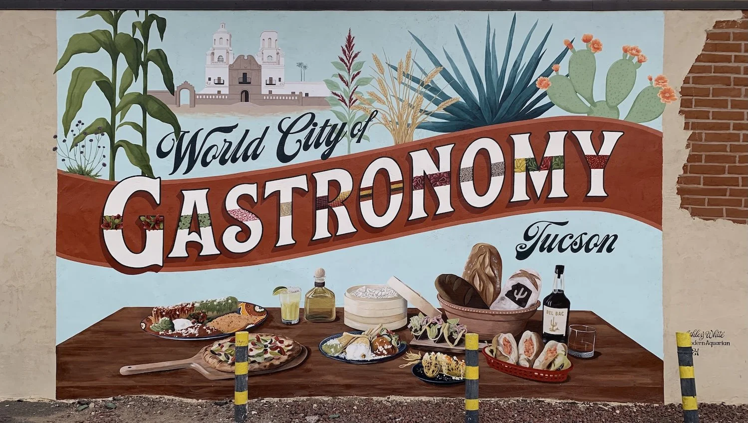"World City of Gastronomy, Tucson"  mural with desert plants, a historic mission, and a table filled with colorful regional foods and drinks.