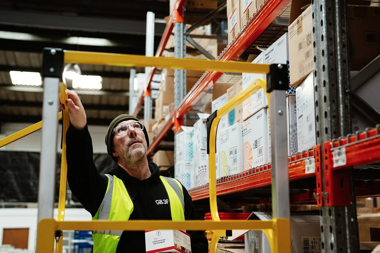 A man in high-vis jacket climbs a step ladder at a warehouse facility in Norwich. 