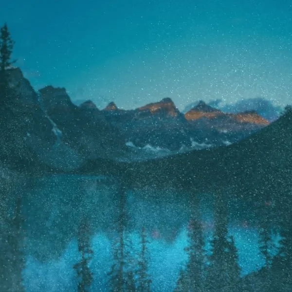 Snow falling over a mountain lake with pine trees in the foreground
