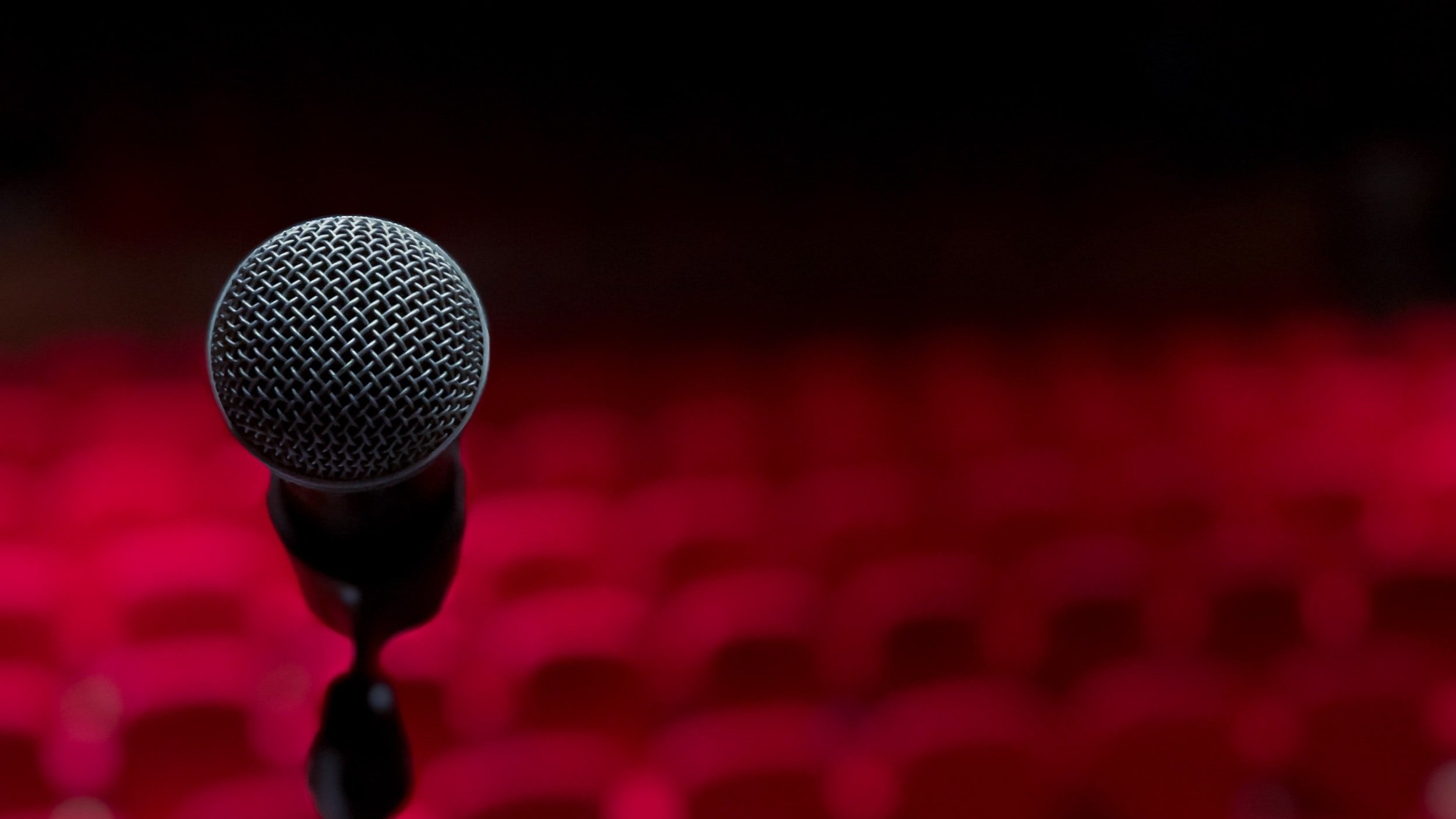 A close-up of a microphone on a stage with a blurred red and black background.